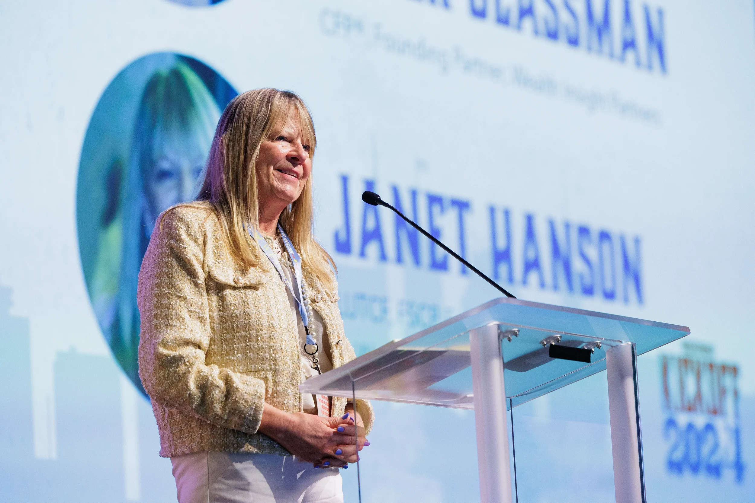 Speaker stands at glass podium smiling with projected introduction slide displayed behind her at Orlando conference