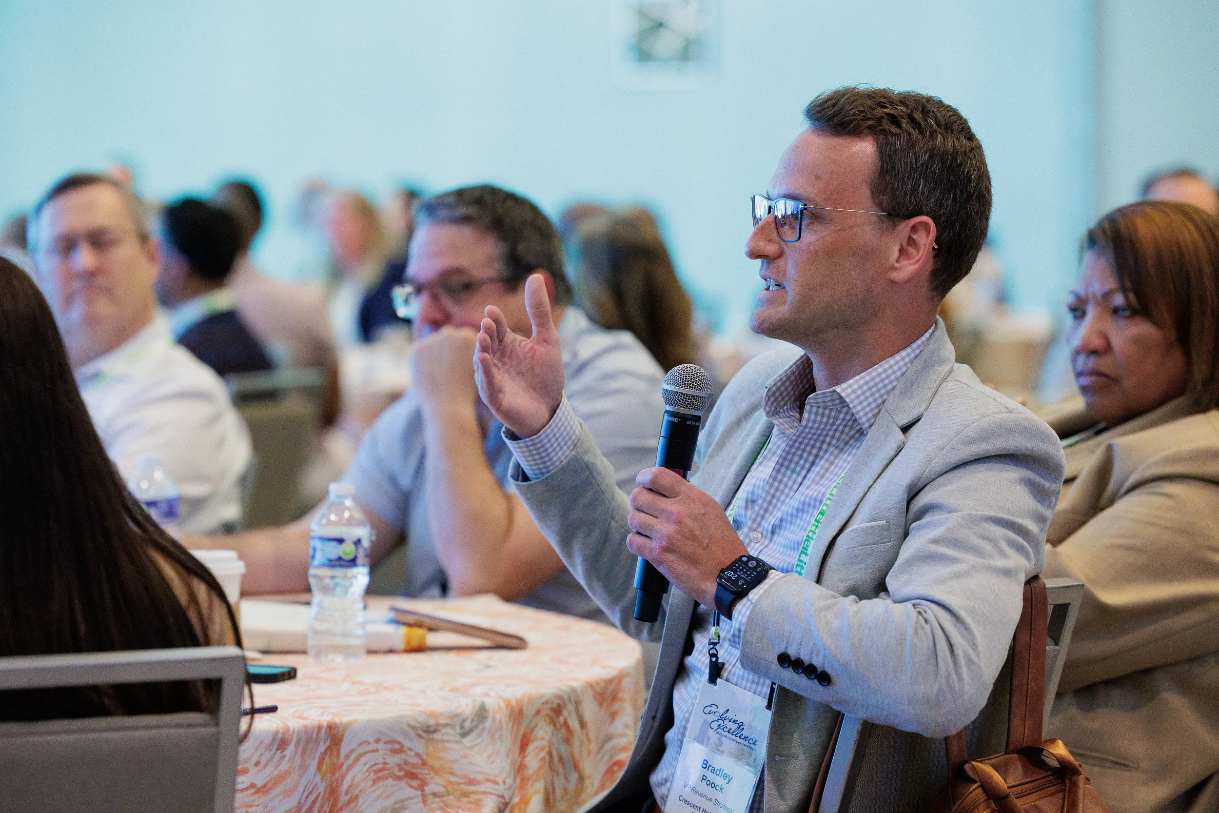 Male attendee holds microphone and gestures while speaking during seated session at Chicago industry conference