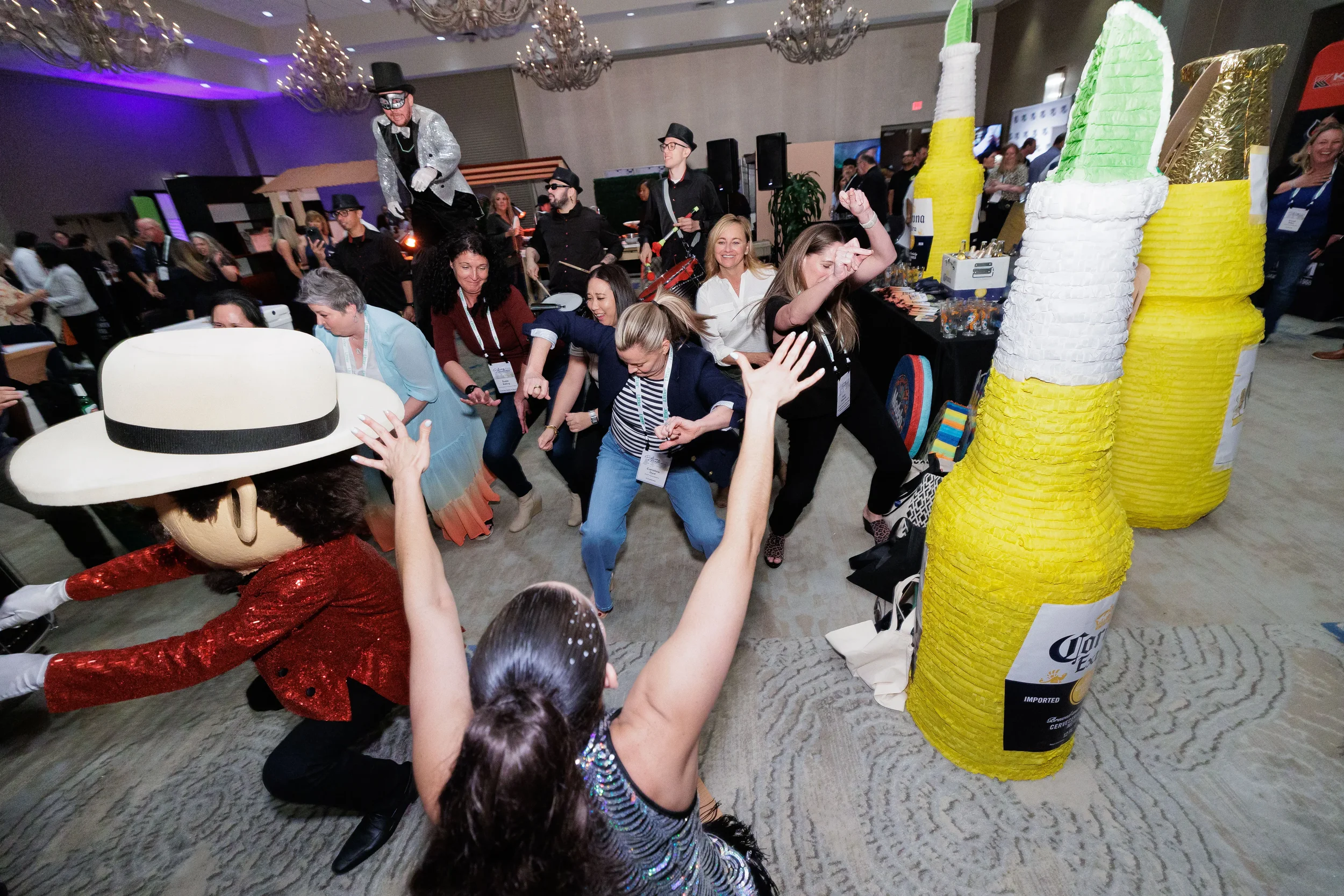 Attendees dance energetically near giant piñata props with stilt performer at Chicago industry conference