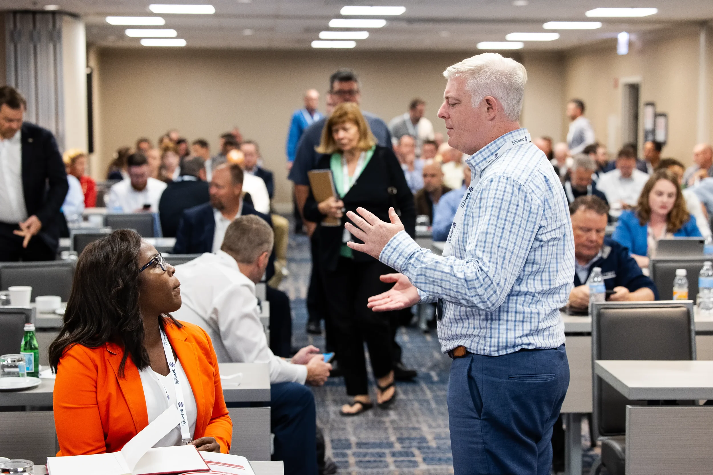 Two conference attendees share a conversation between sessions in a busy Orlando conference room