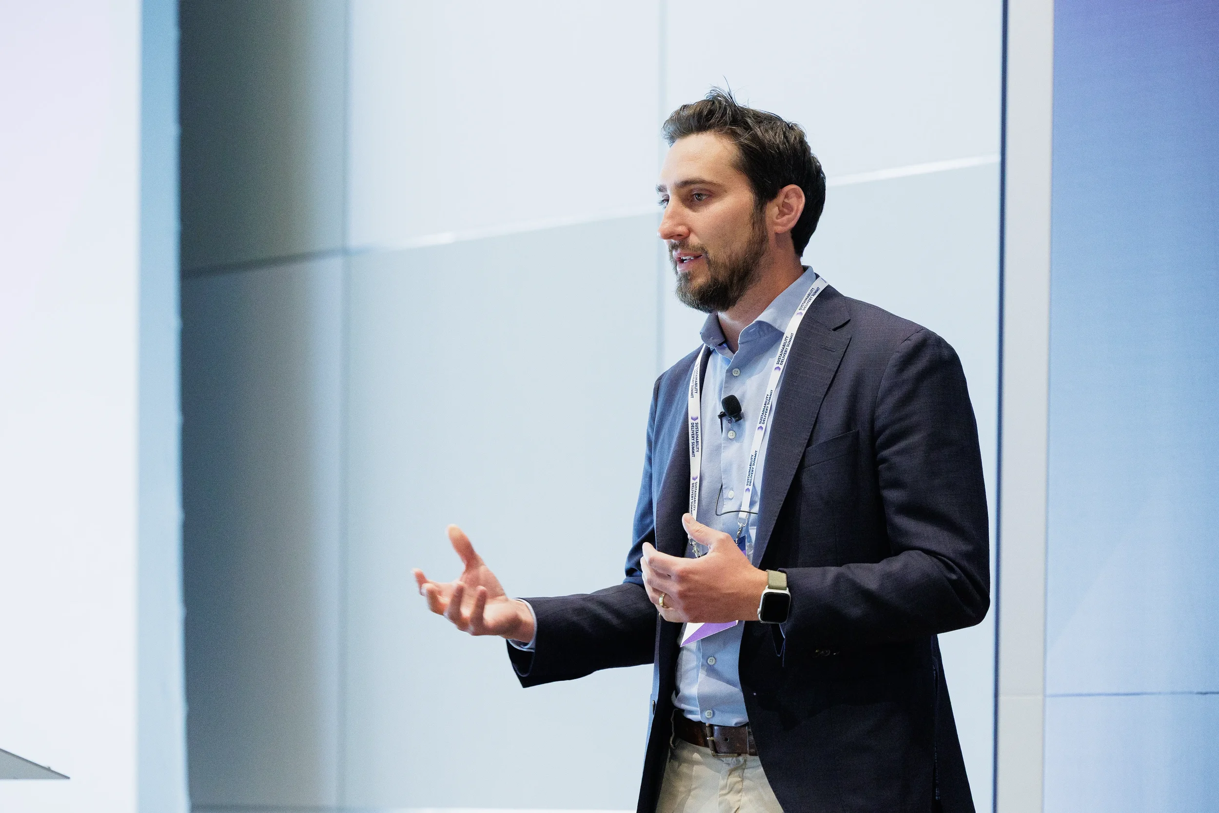 Speaker gestures while presenting on stage in navy blazer at Chicago corporate event
