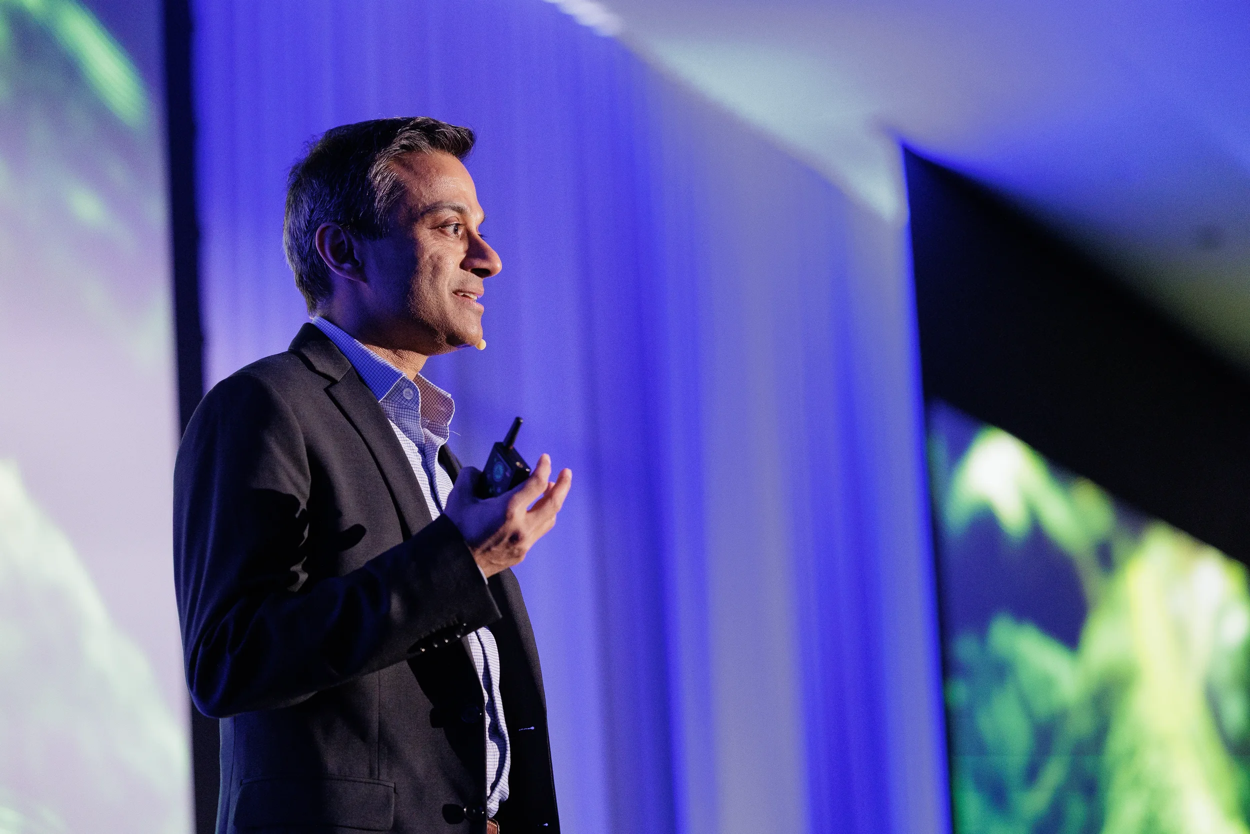 Speaker in profile with headset microphone and clicker presents on stage at Orlando industry conference