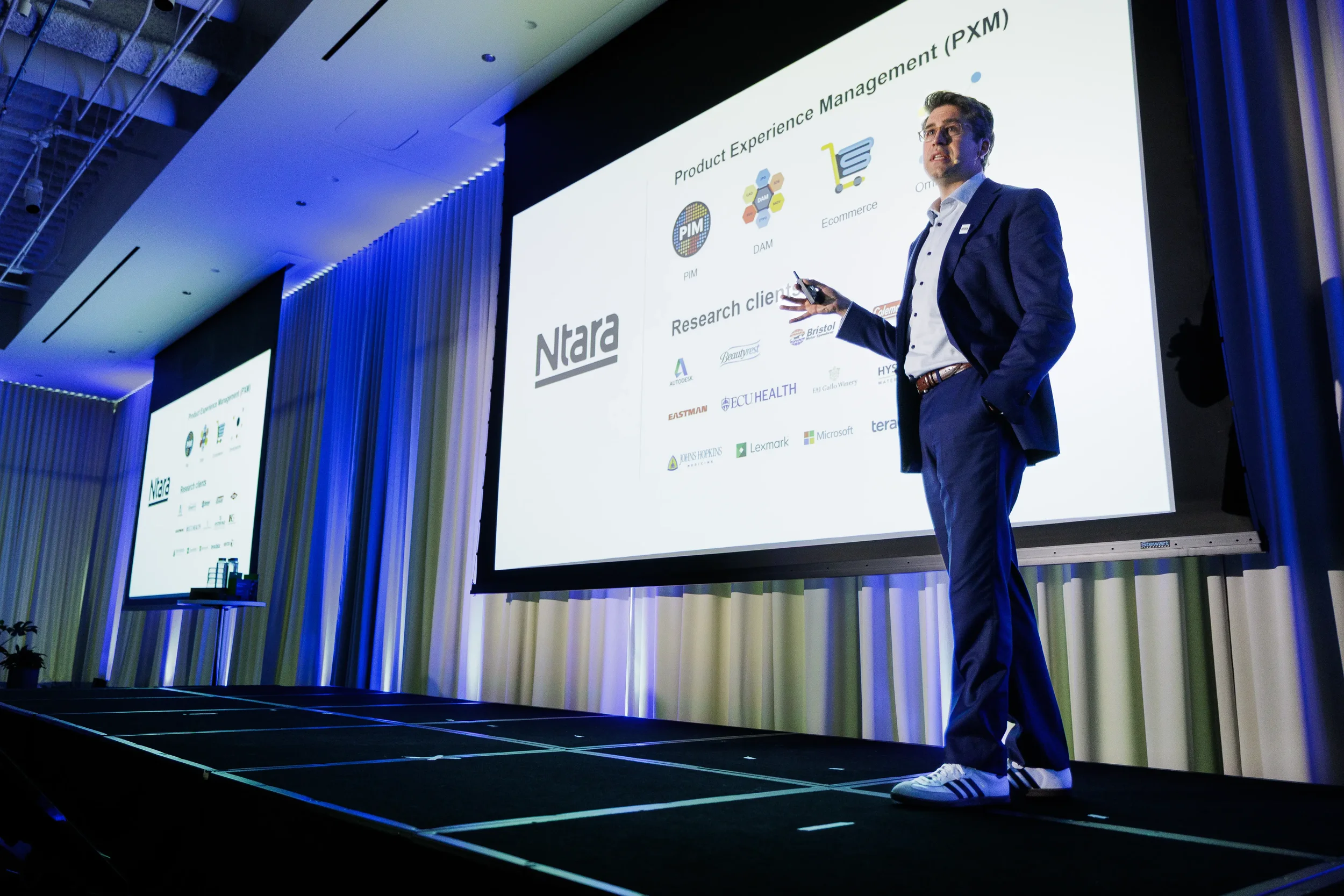 Speaker in blue suit presents beside large projection screen on stage at Chicago industry conference