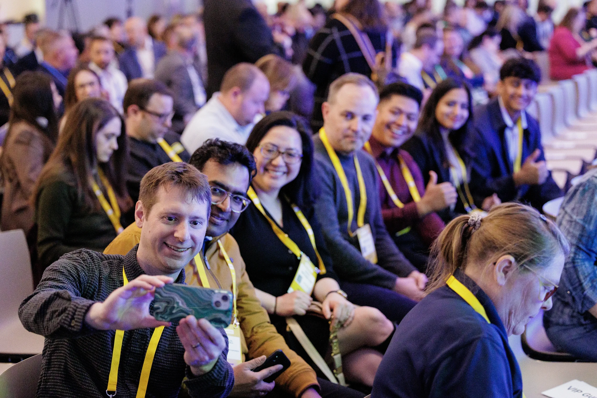 Smiling attendees take group selfie in seated audience before session at Orlando industry conference