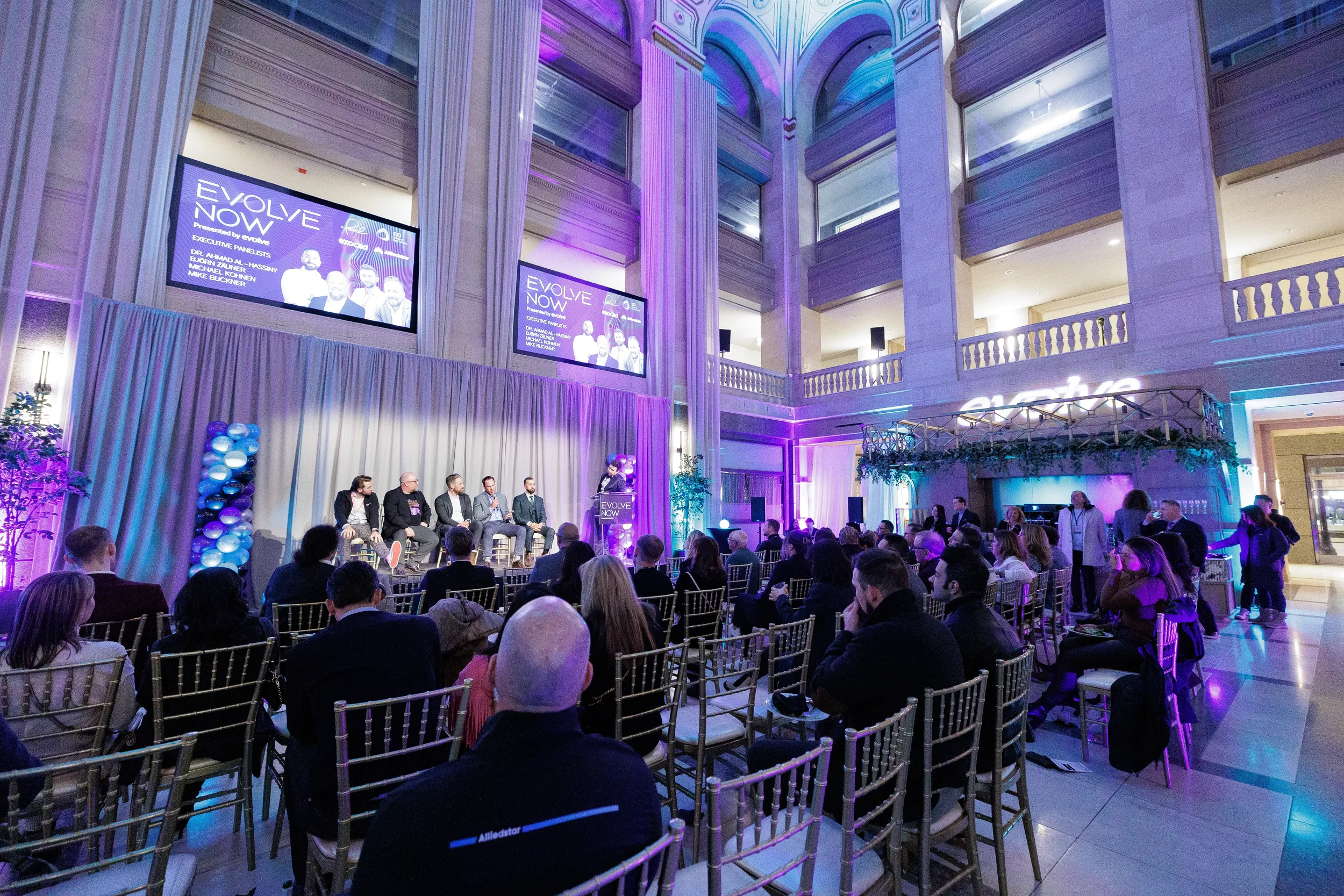 Wide shot of panel on stage with full seated audience in grand atrium at Orlando corporate event