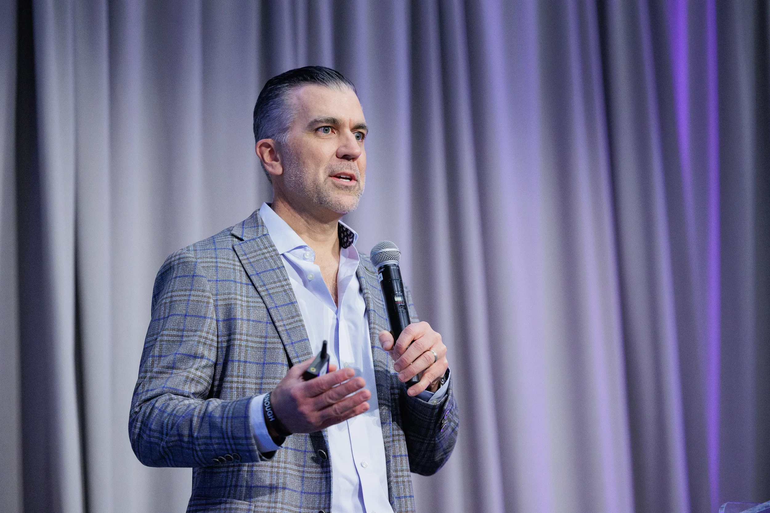 Speaker in plaid blazer gestures while presenting with microphone at Chicago corporate event