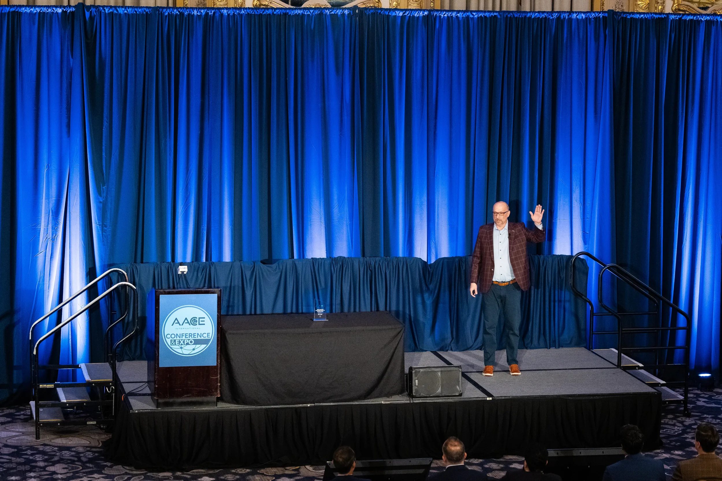 Keynote speaker waves to audience from ballroom stage during Chicago conference general session