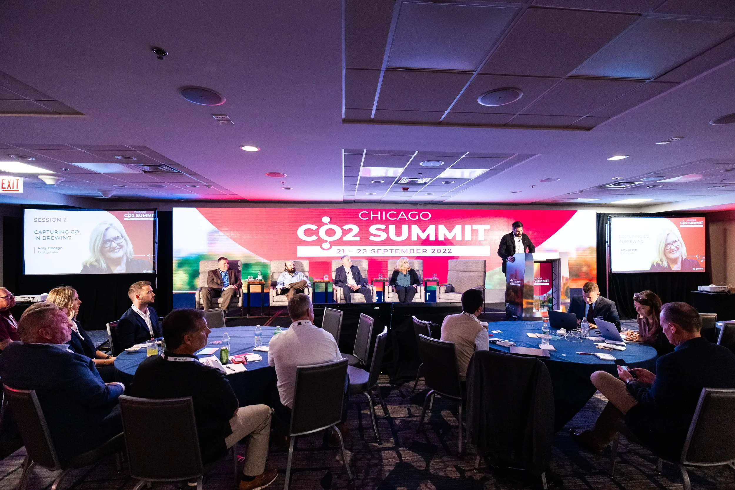 Wide view of audience seated at round tables during panel discussion at Orlando industry conference