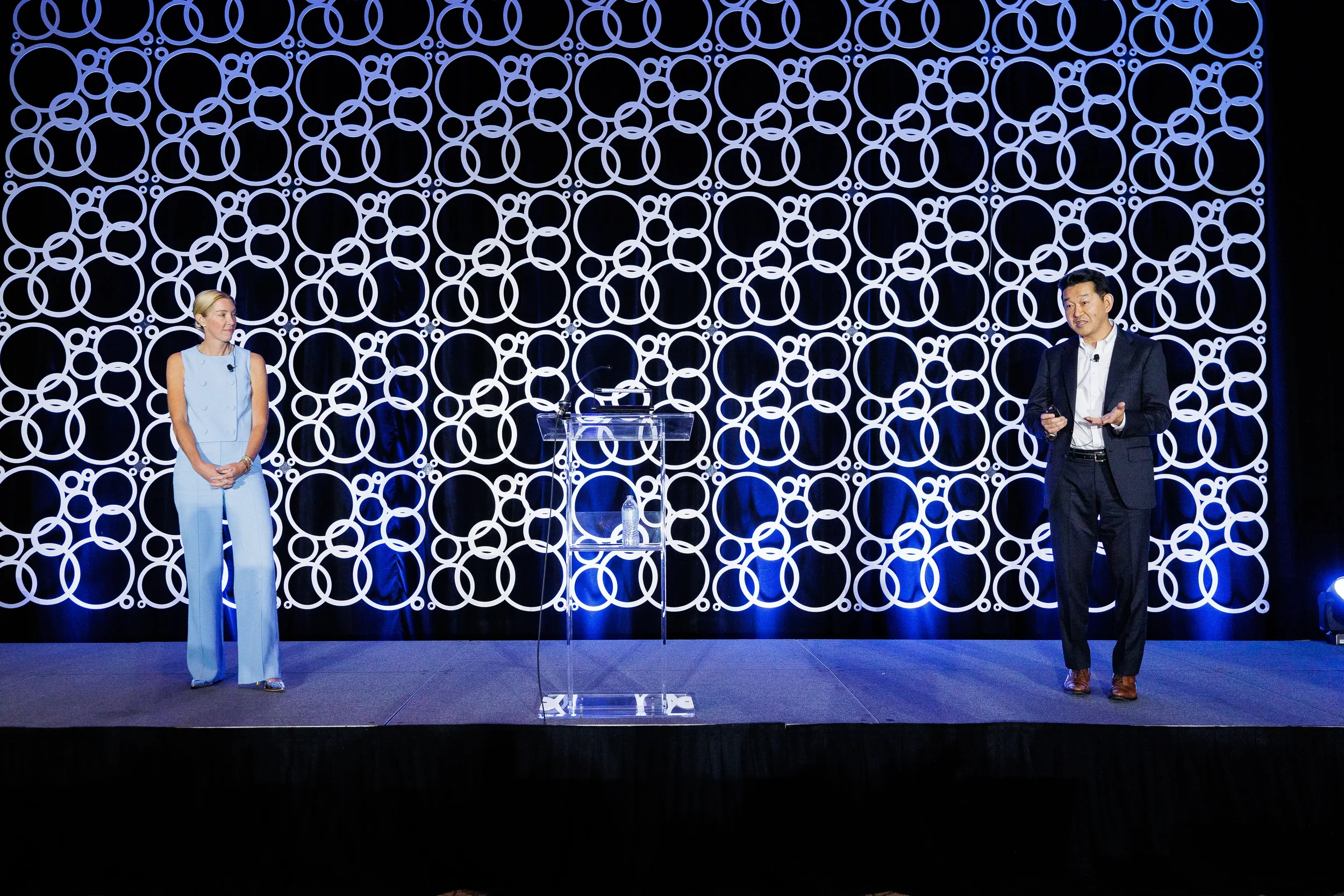 Two speakers present on stage with branded circle backdrop at Chicago conference