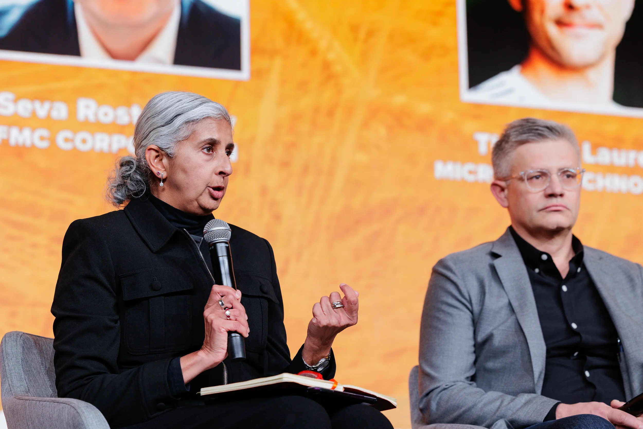 Female panelist with gray hair holds microphone and gestures on stage at Chicago industry conference