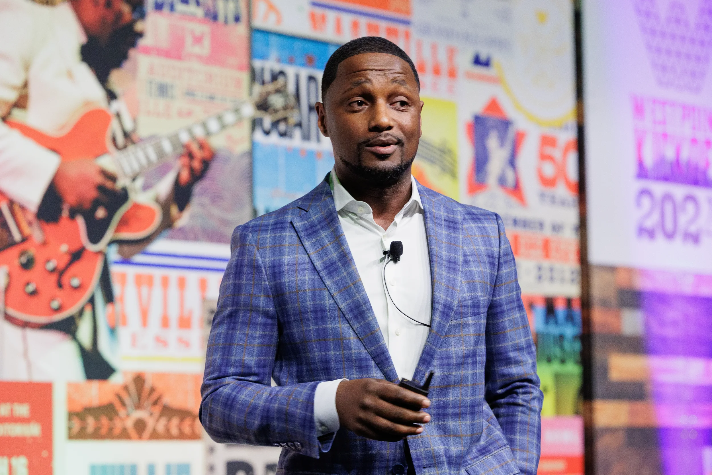 Keynote speaker in blue plaid jacket addresses audience in front of colorful branded backdrop at Chicago corporate conference