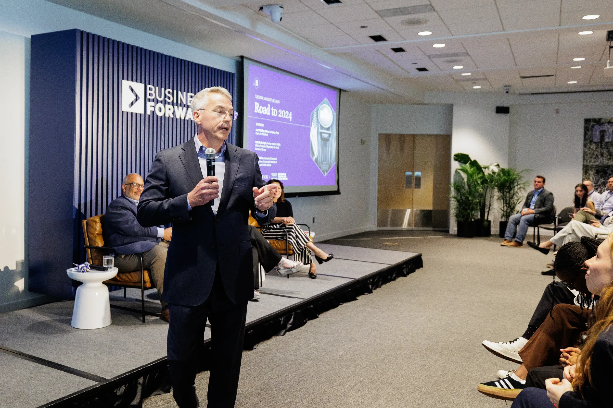 Speaker addresses audience with microphone while panelists sit on stage at Chicago corporate event