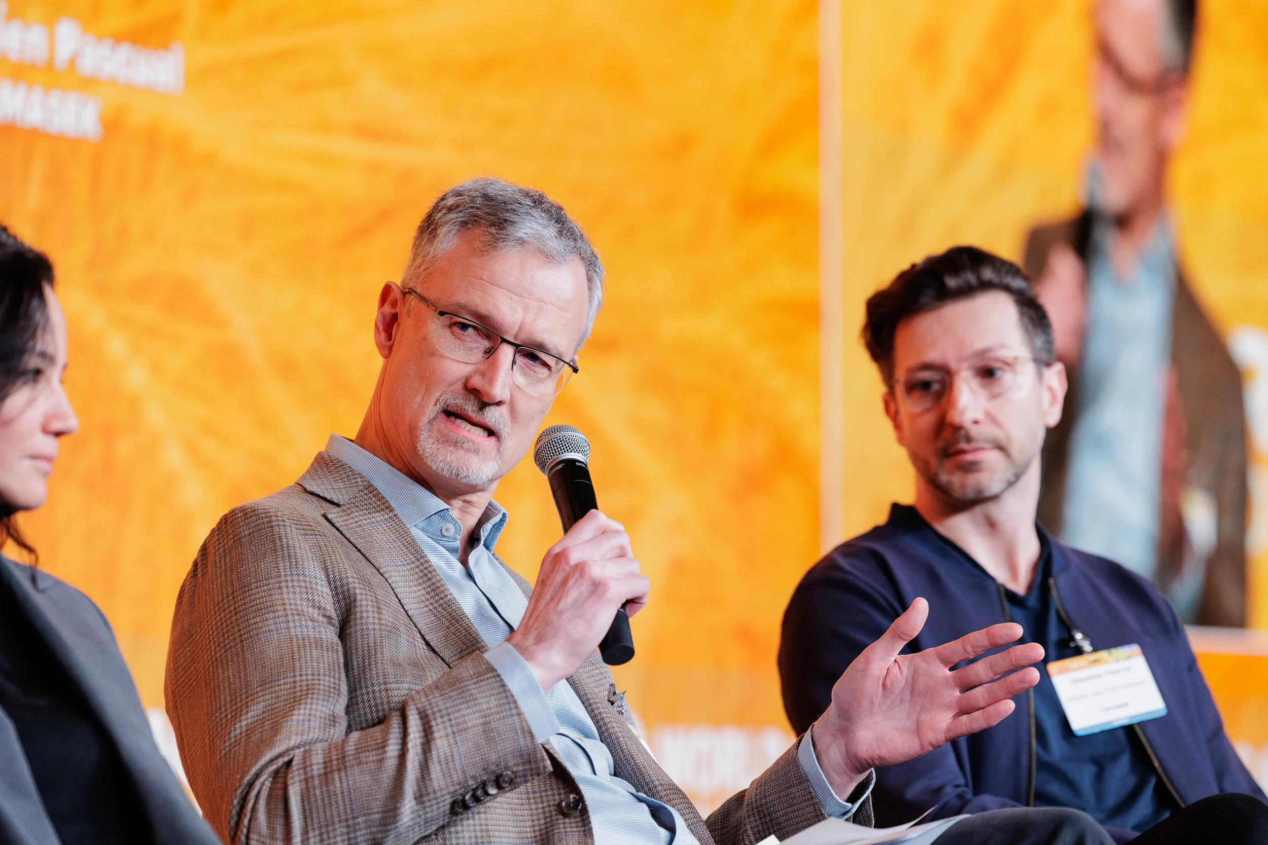 Male panelist in tweed jacket speaks into microphone and gestures at Chicago corporate event