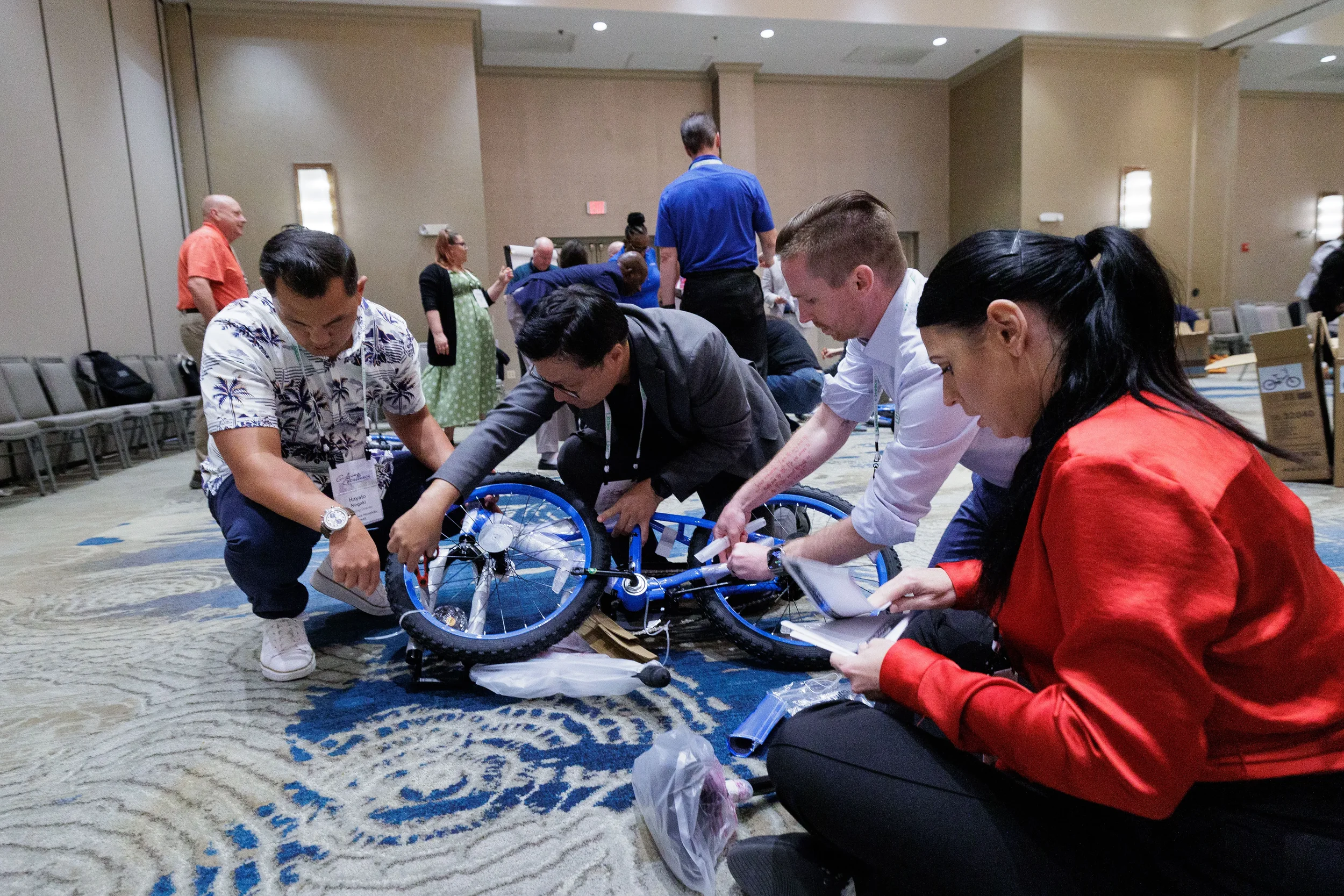 Attendees kneel on ballroom floor assembling a bicycle during team activity at Orlando corporate event