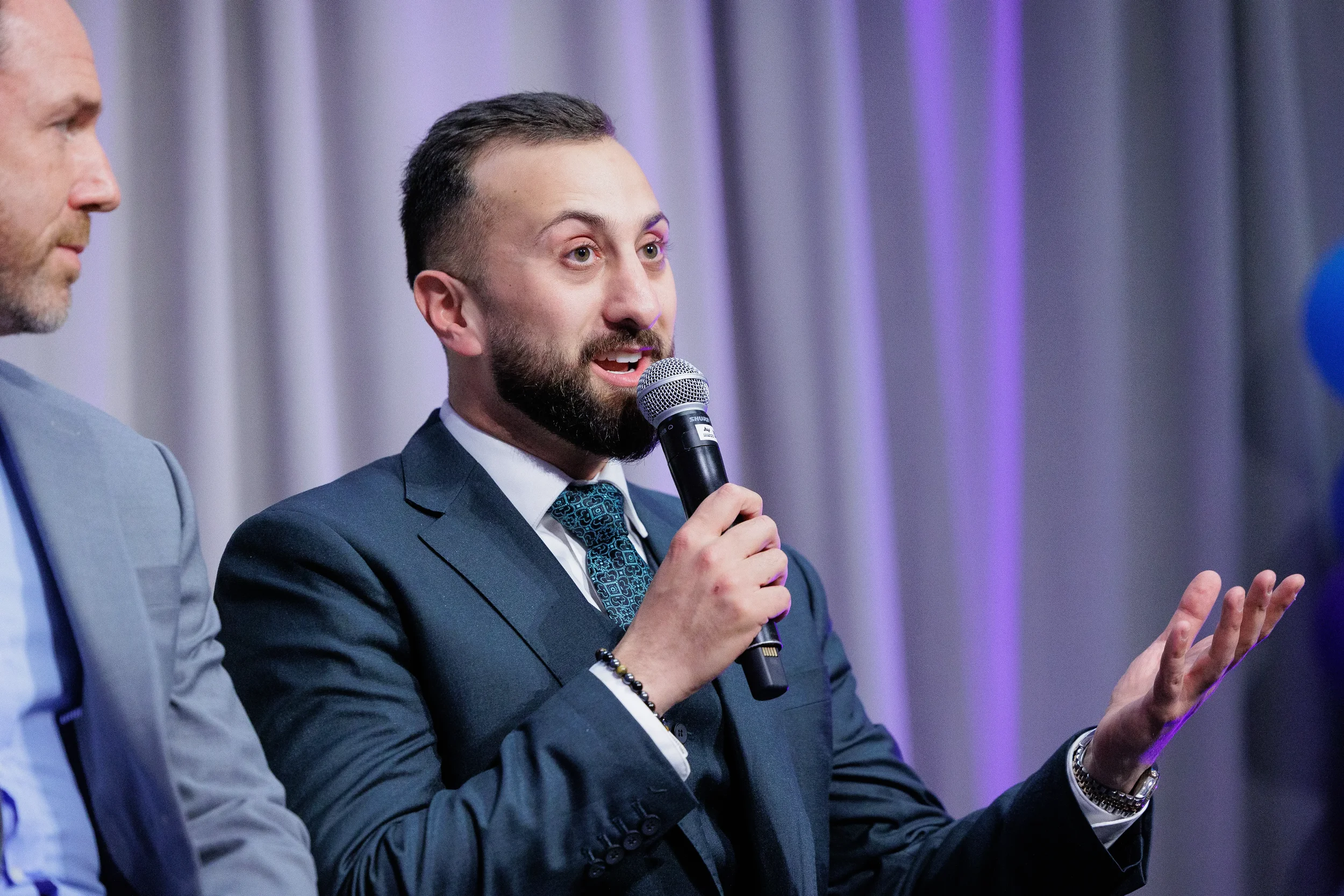 Suited panelist speaks into microphone while gesturing during panel discussion at Orlando industry conference