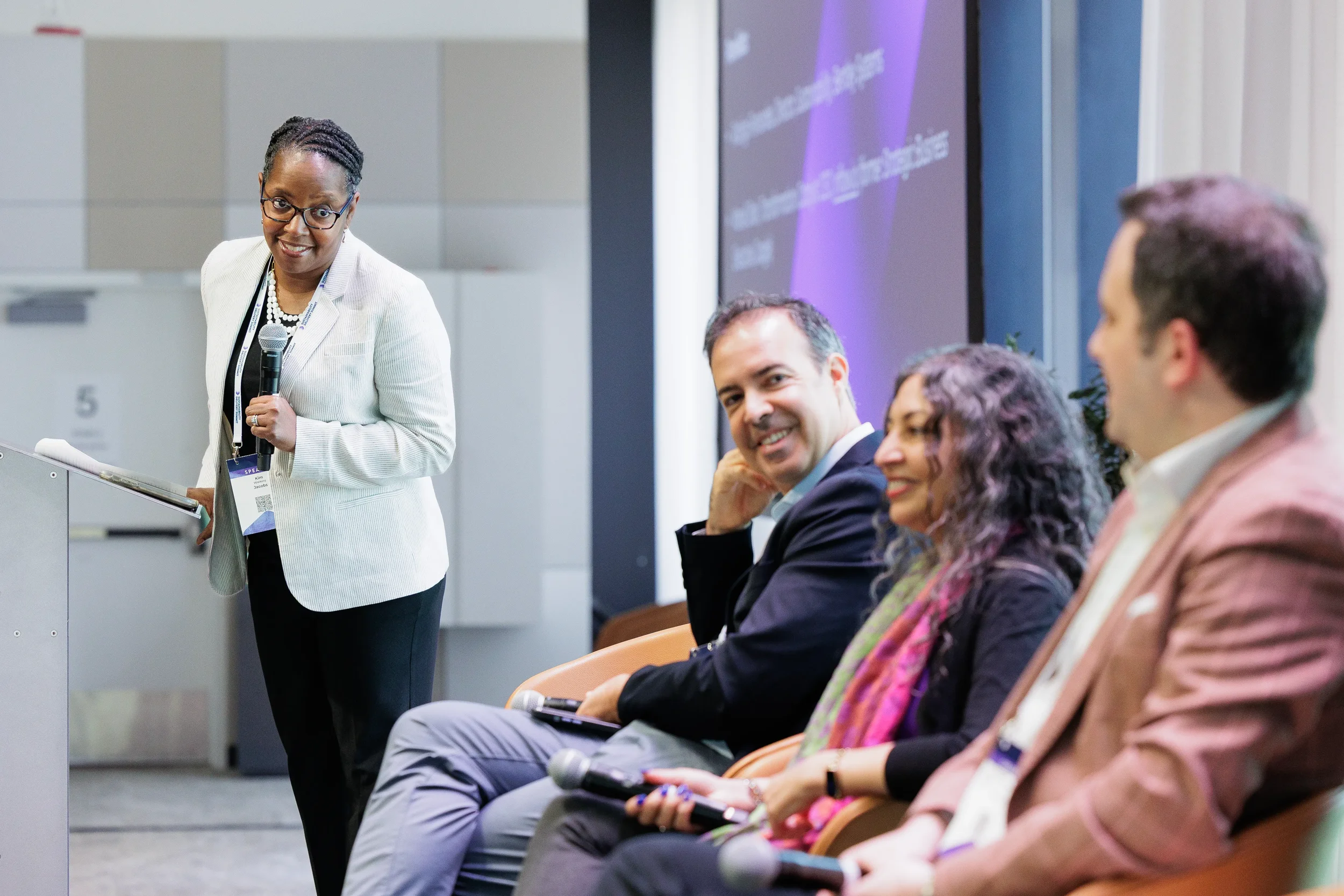 Speaker holds microphone while addressing seated panelists during Chicago industry conference session