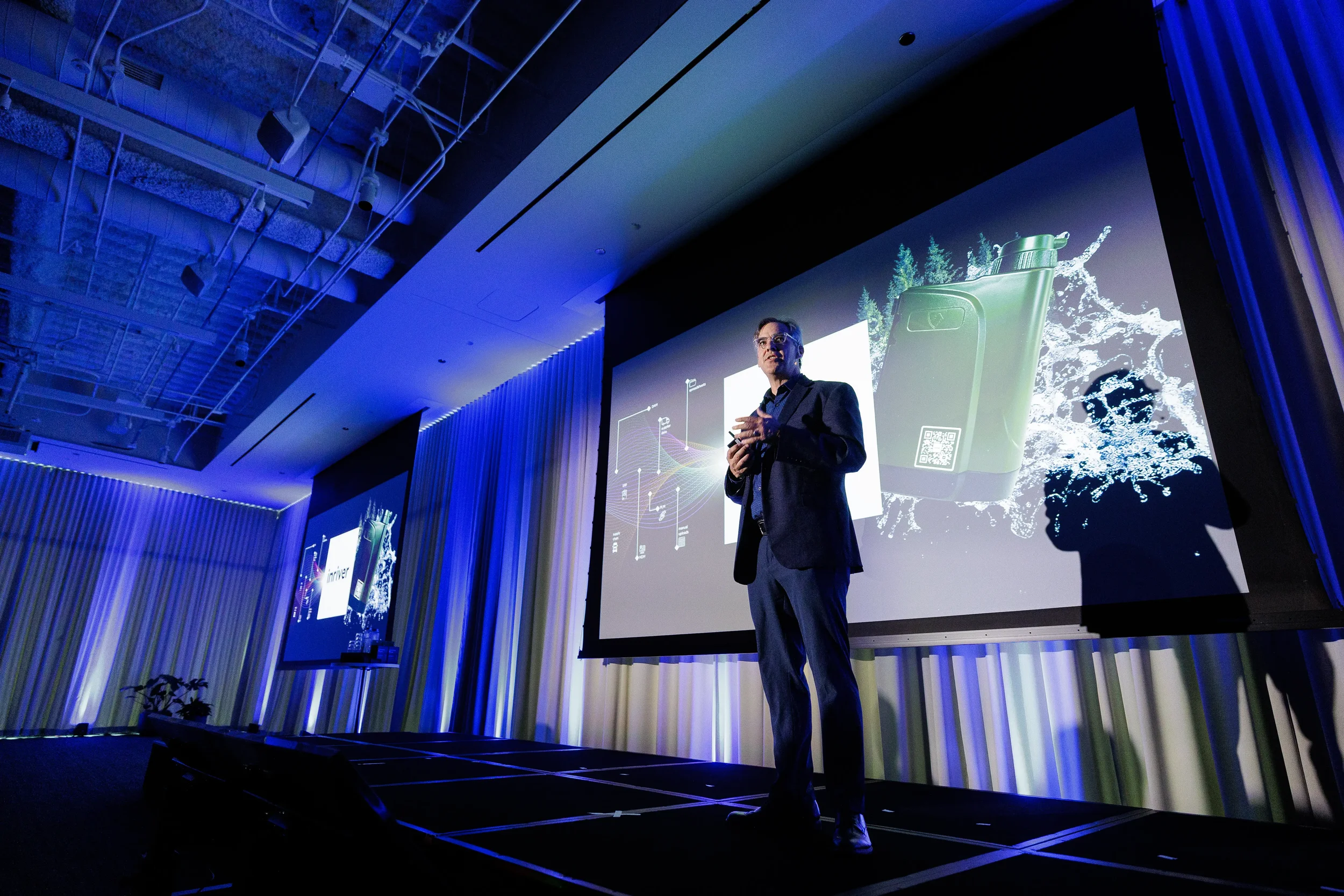 Speaker presents product slide on stage with blue curtain lighting at Chicago industry conference