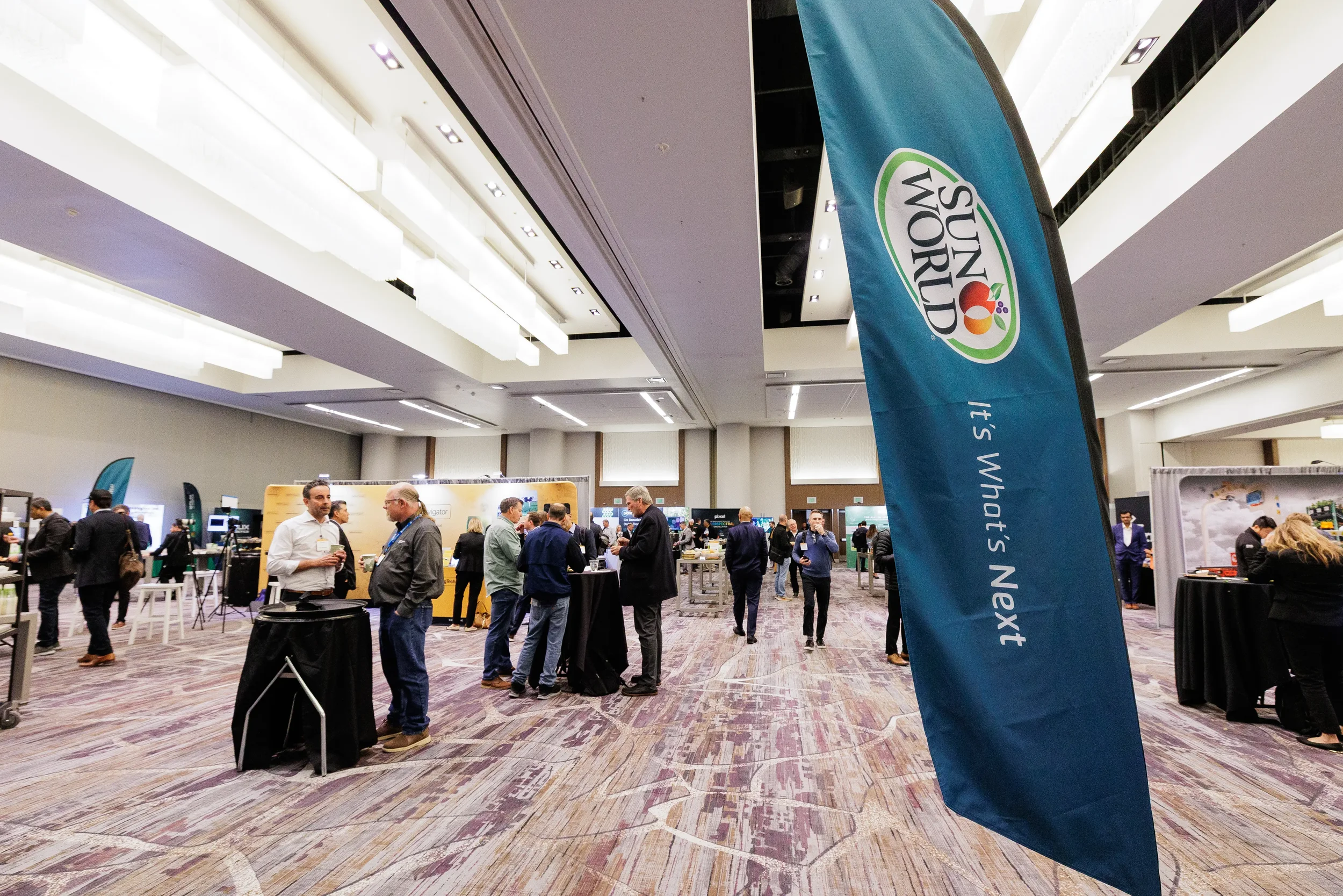 Attendees gather among exhibitor booths and sponsor banner on Orlando expo floor