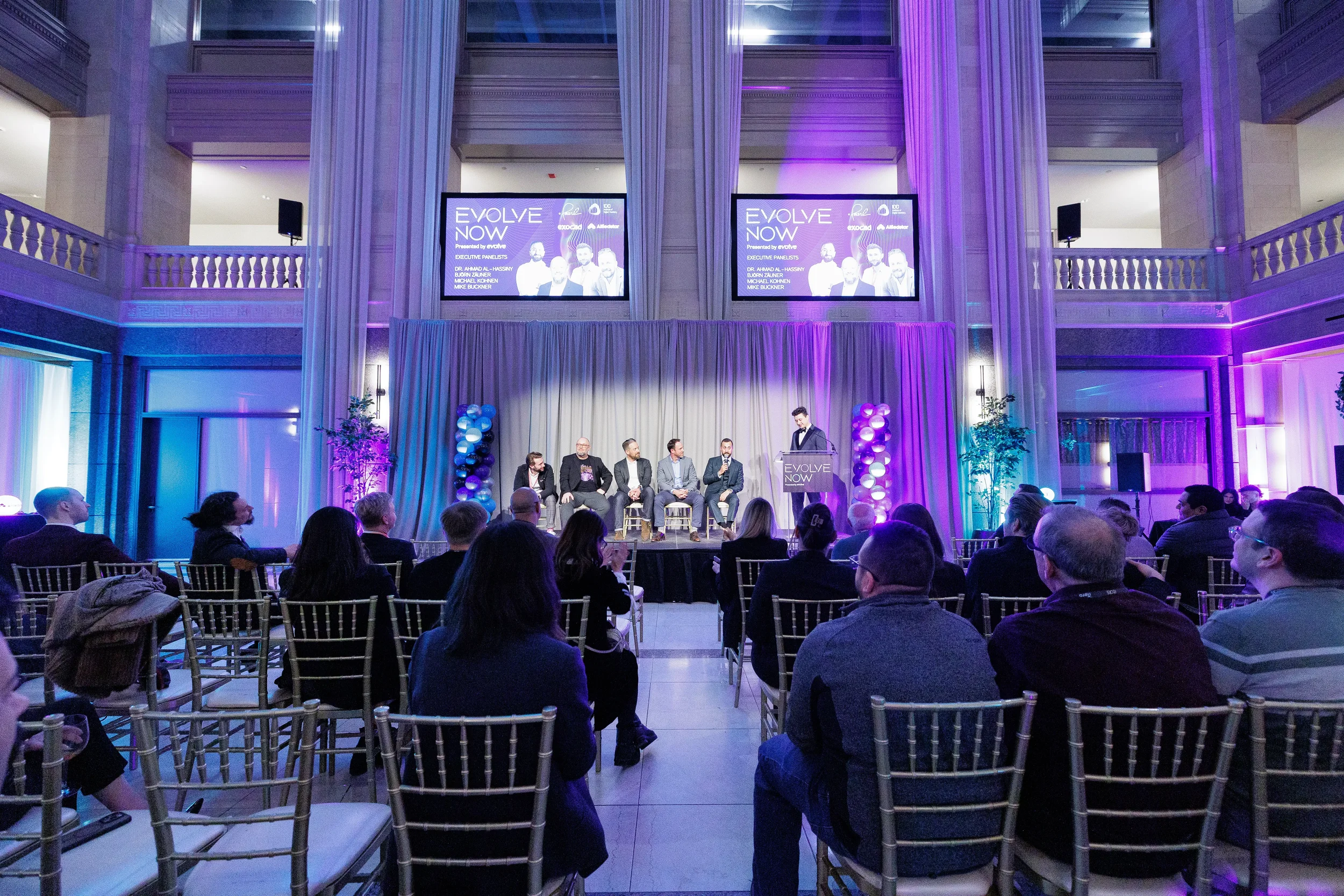 Full audience watches panel of speakers on stage beneath dual screens at Orlando industry conference