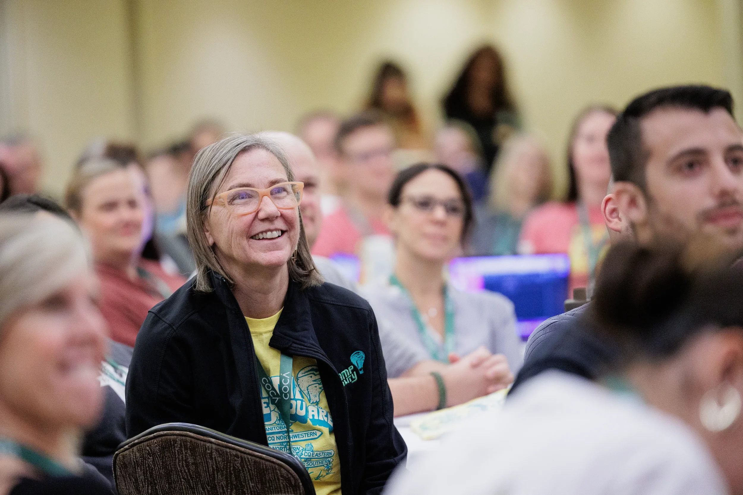 Attendee wearing conference lanyard smiles while watching session among packed crowd at Orlando nonprofit conference