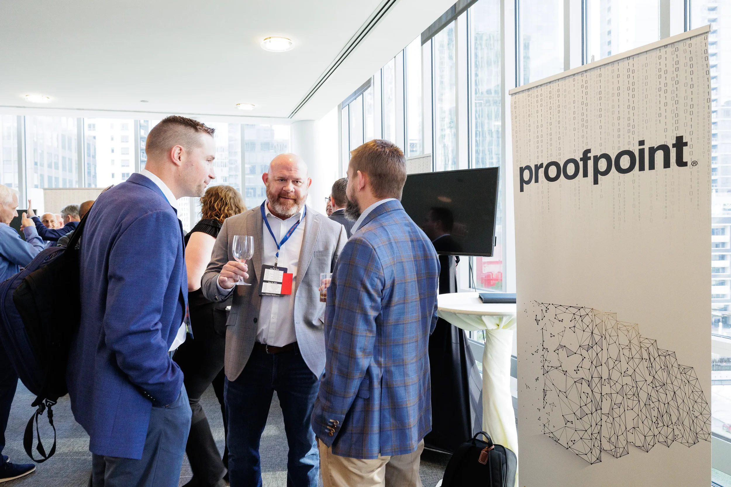 Three male attendees with drinks converse near sponsor banner during Chicago corporate conference reception