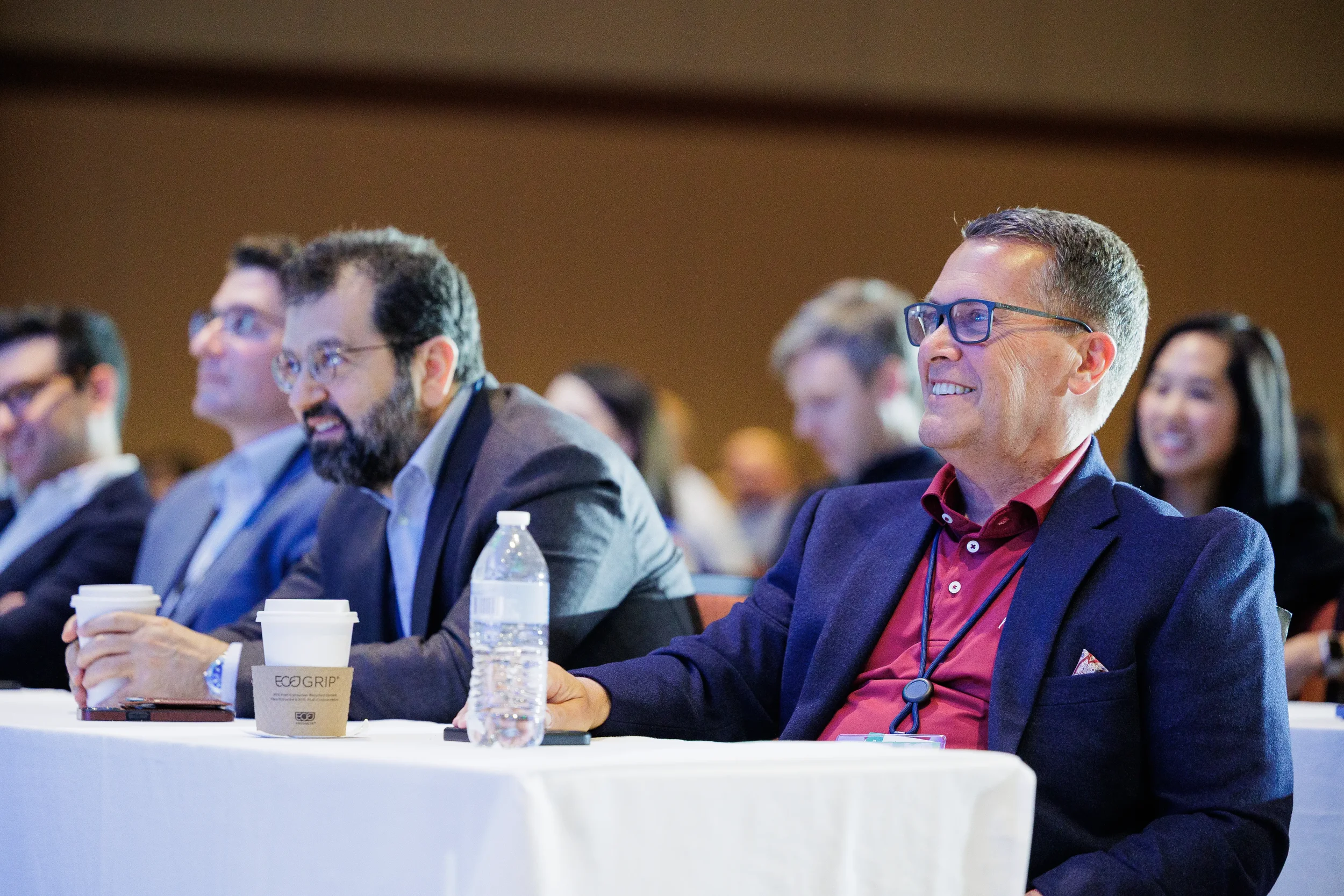 Attendees laugh and listen at front-row table with coffee during Orlando industry conference