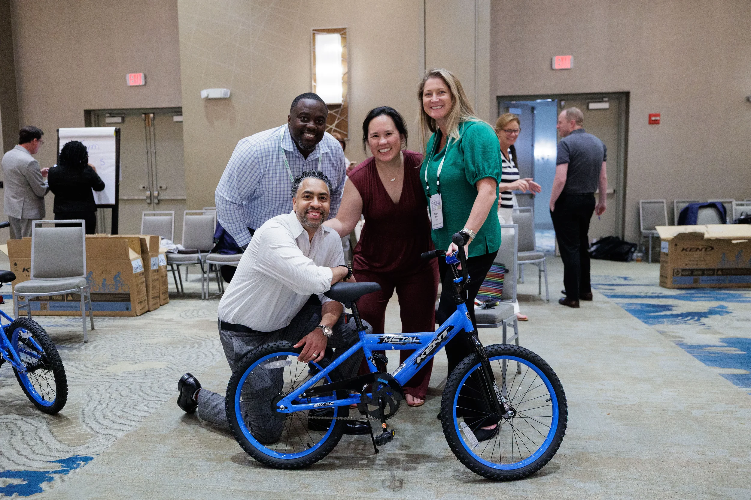Four smiling attendees pose with completed blue bicycle during team building activity at Orlando corporate conference