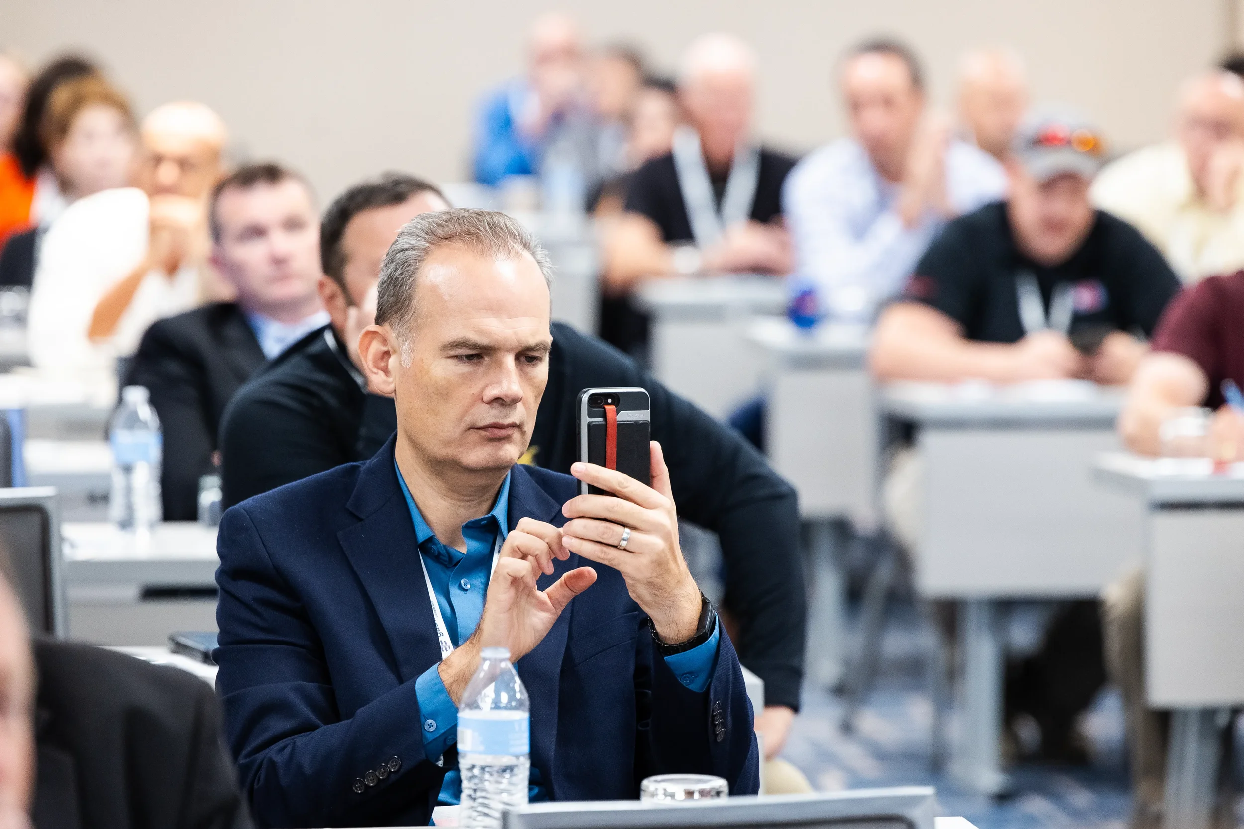 Conference attendee photographs presentation on smartphone during session at Orlando industry event