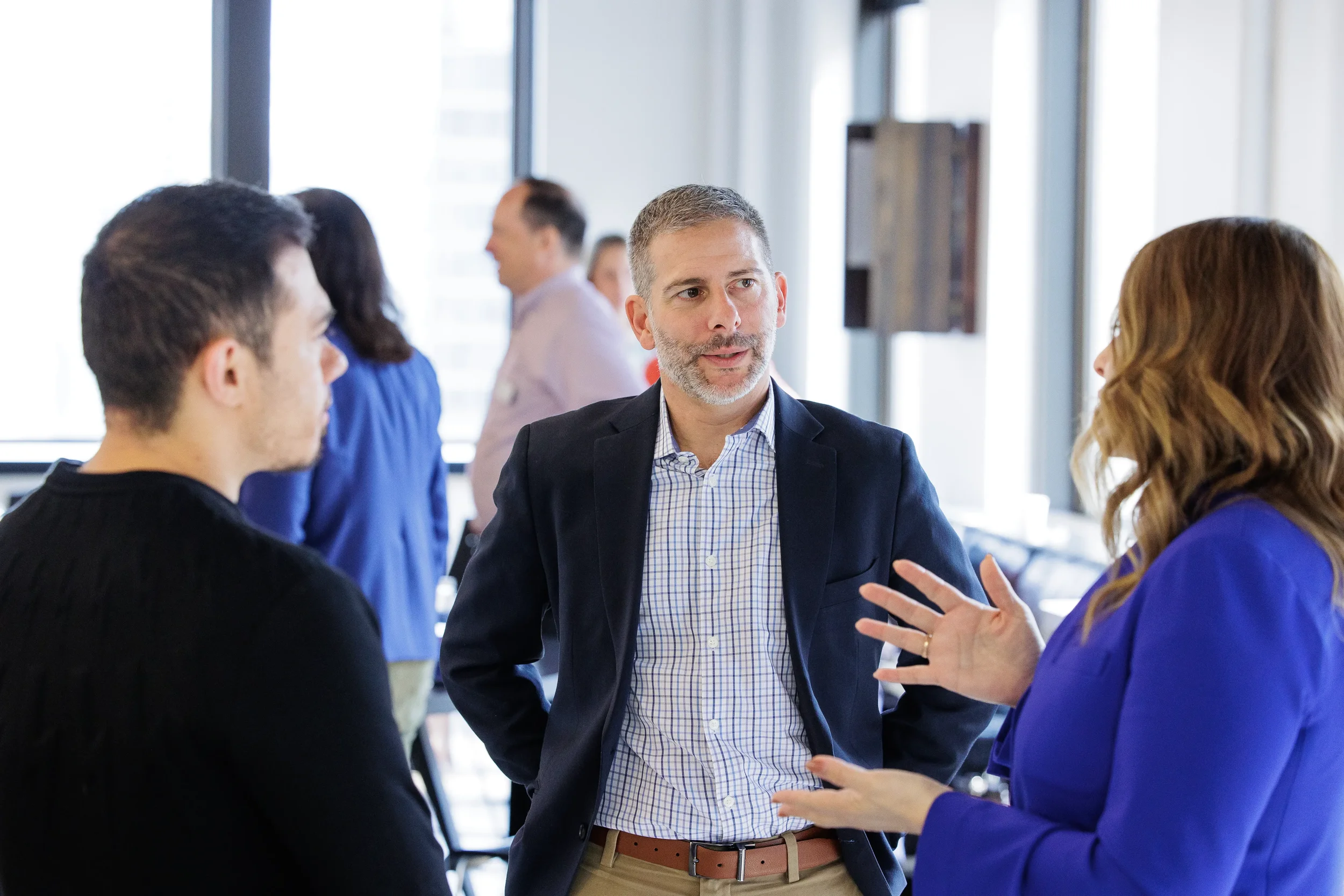 Three business professionals speak during an indoor networking event in Orlando with other blurred figures in the background.