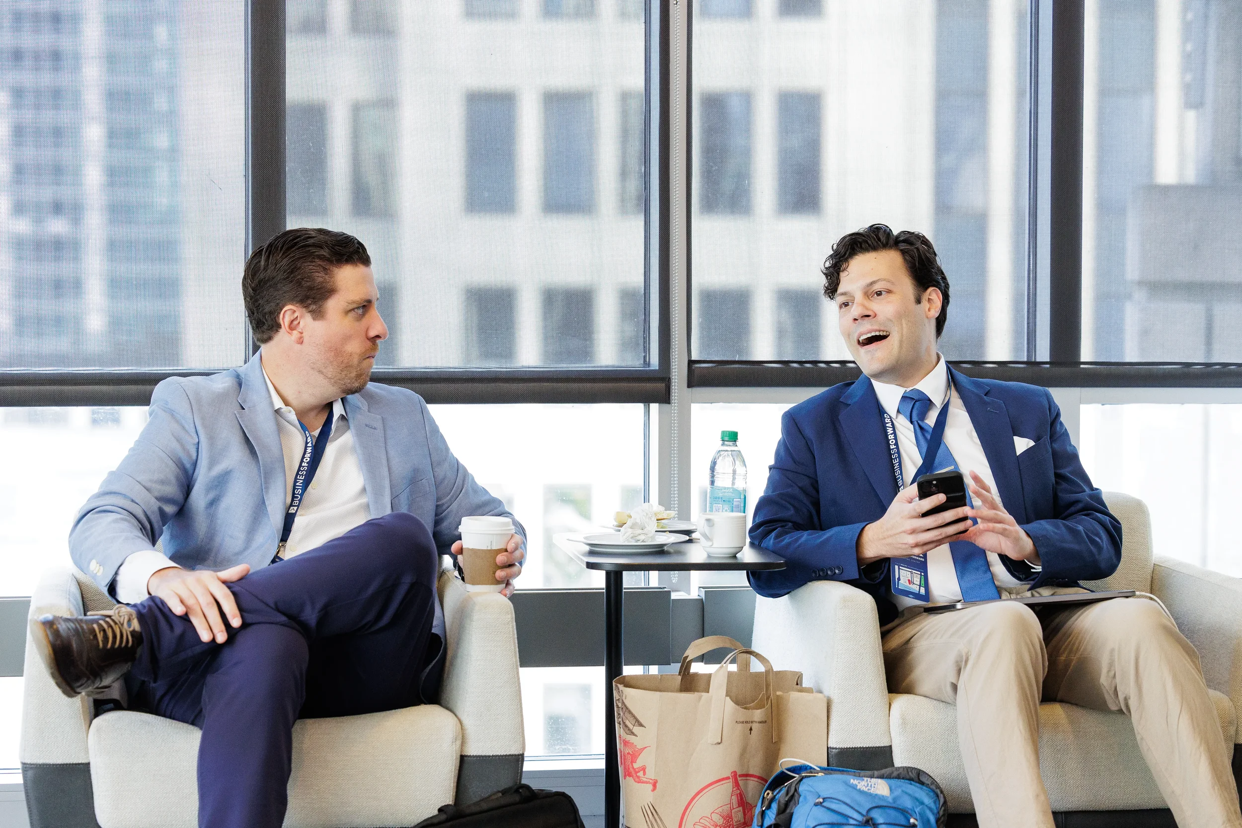 Two attendees chat over coffee in lounge seating area with city skyline views at Chicago conference