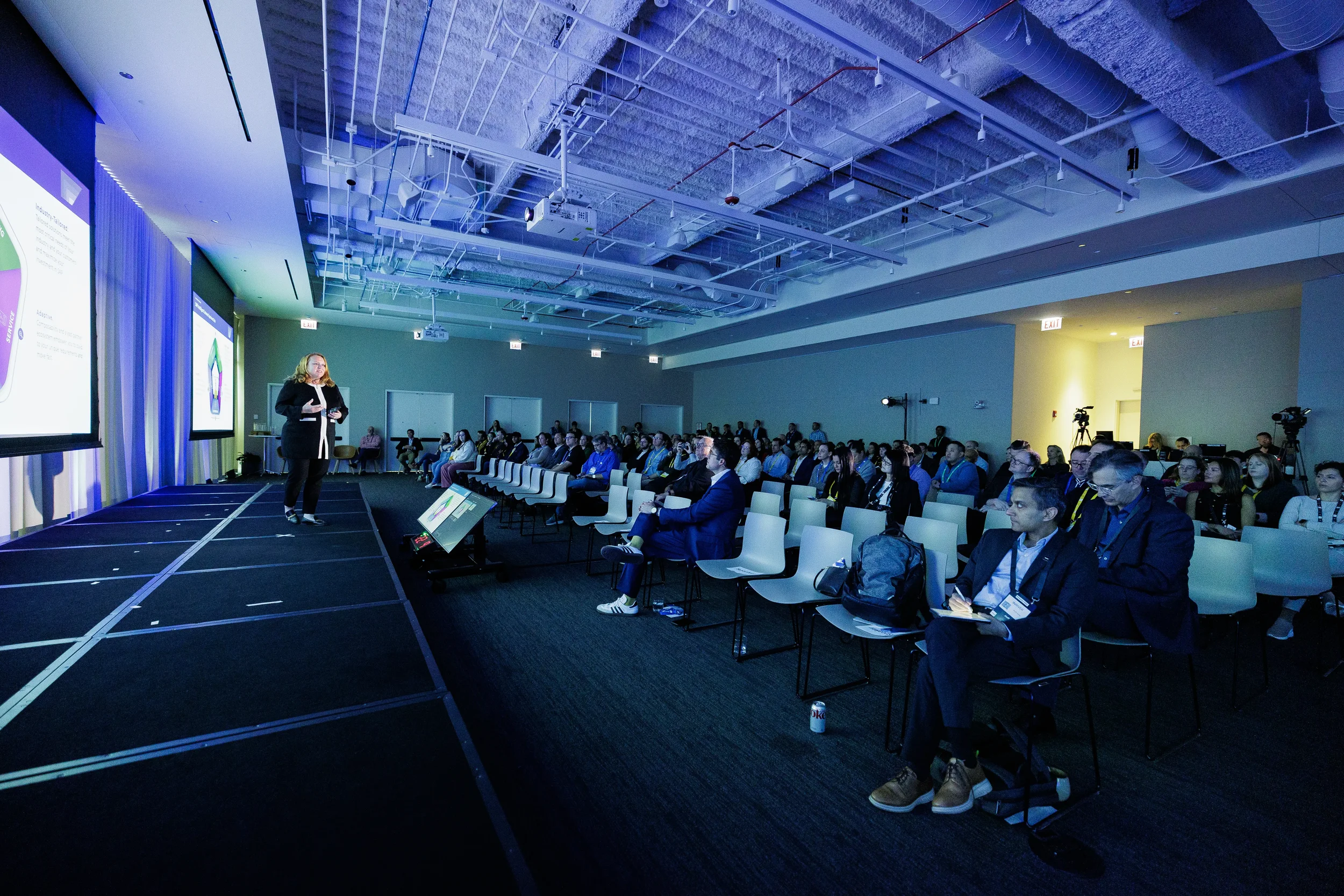Speaker presents on stage to seated audience in blue-lit room at Orlando industry conference