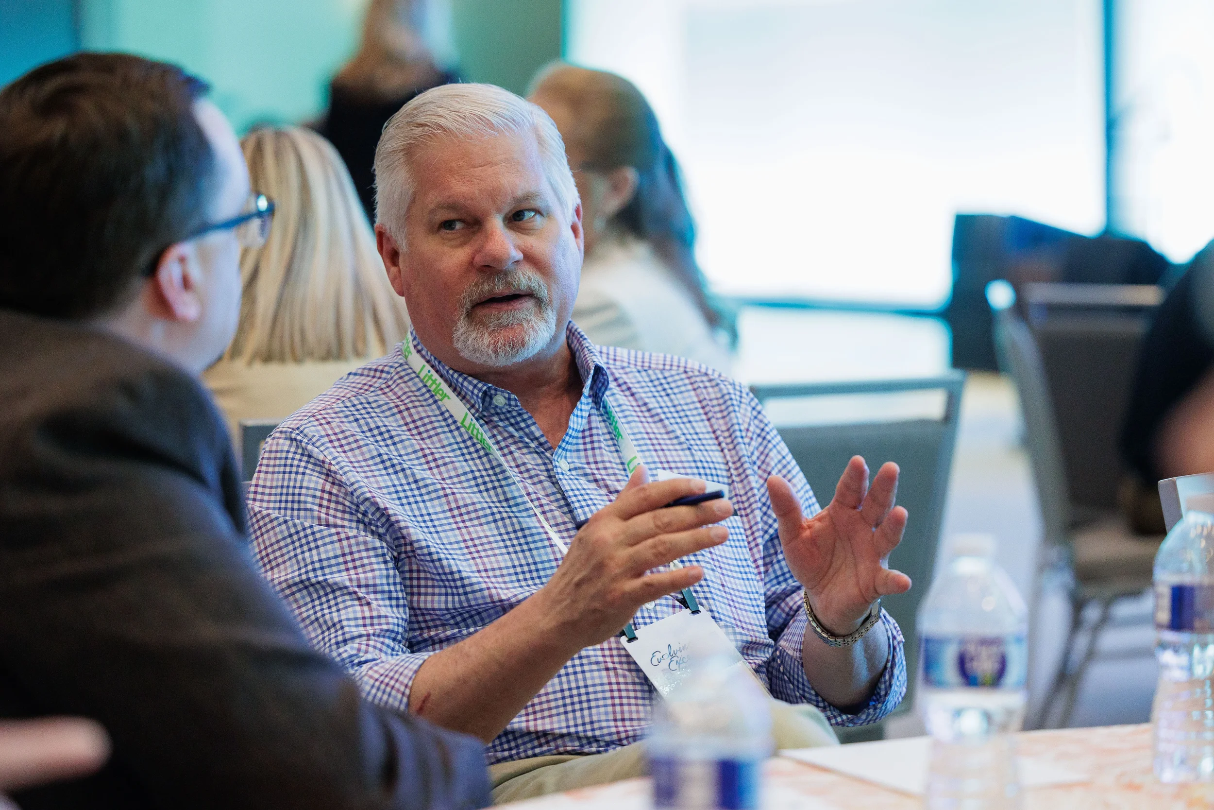 Male attendee with lanyard gestures expressively during table discussion at Orlando industry conference