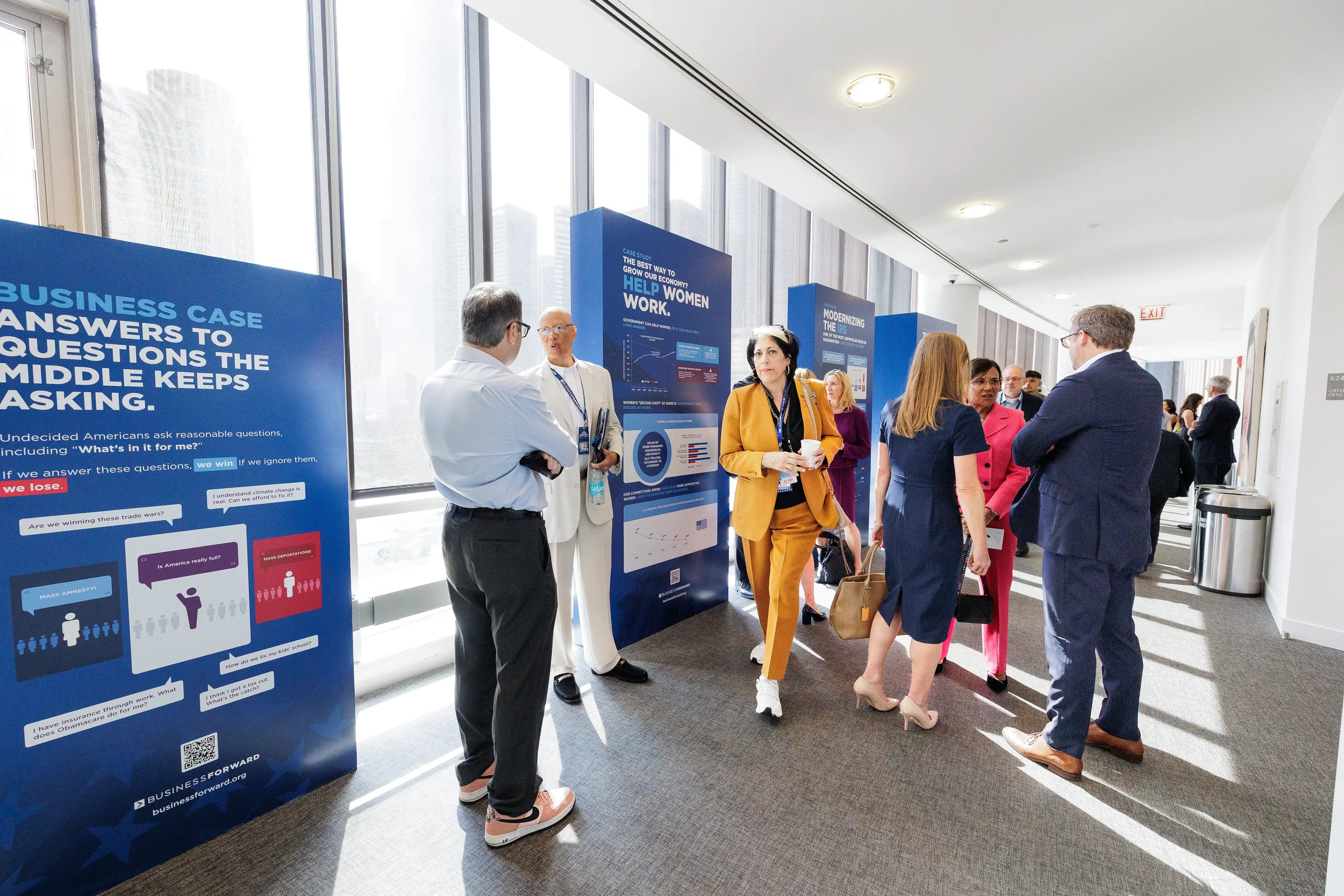 Attendees network in sunlit hallway beside informational displays at Chicago conference venue