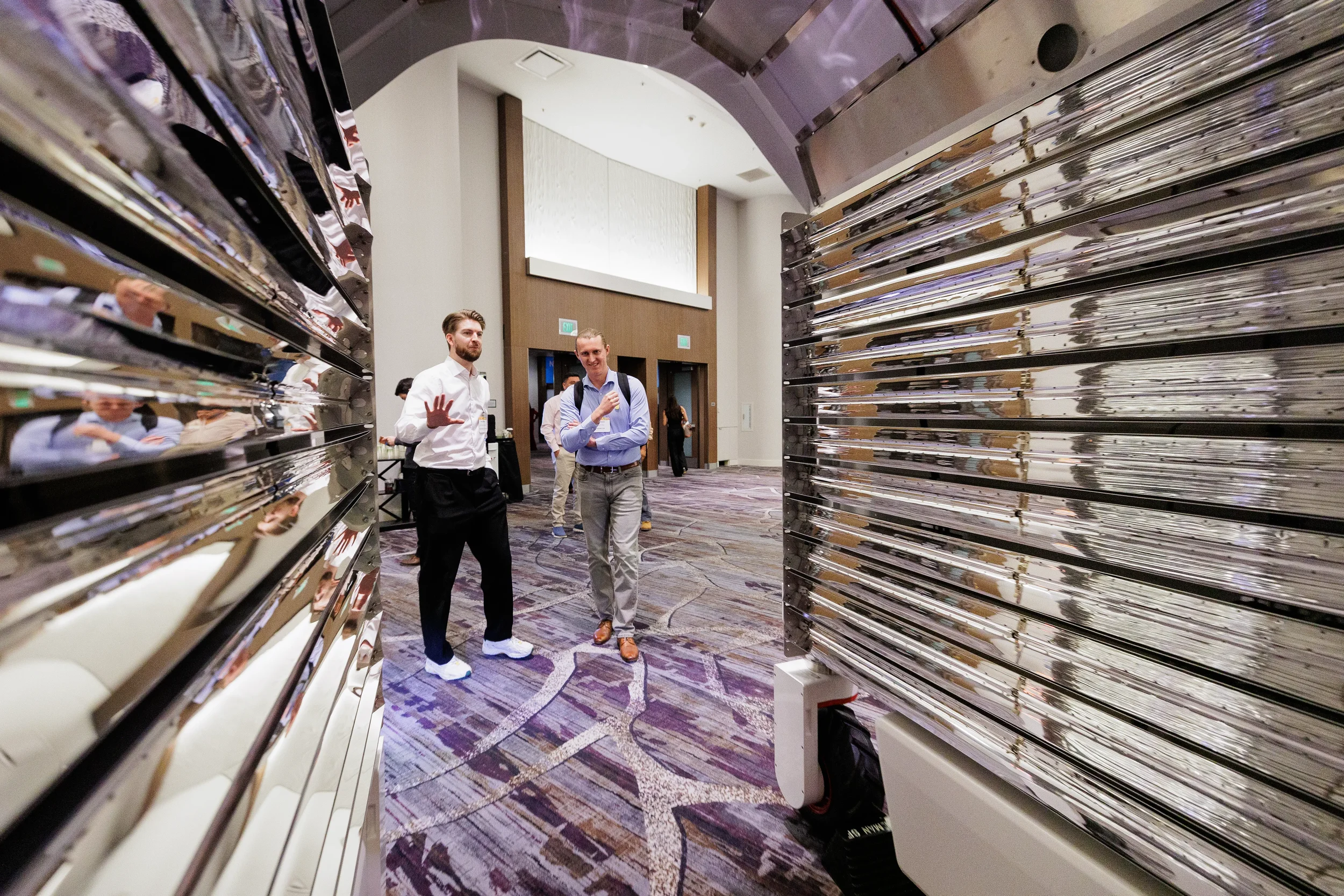 Two attendees stand between large reflective equipment display on Chicago industry conference expo floor
