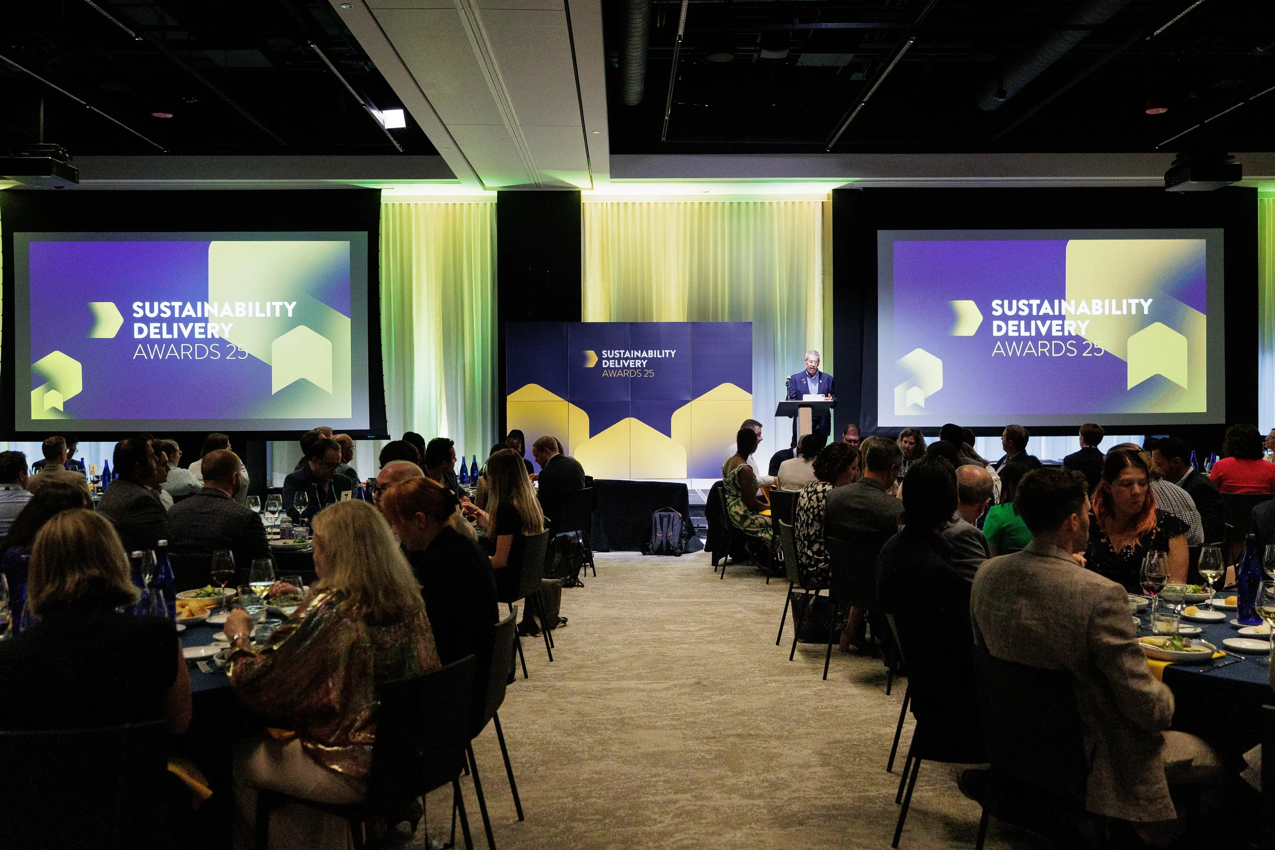 Wide view of awards dinner with speaker at podium and attendees seated at Orlando conference