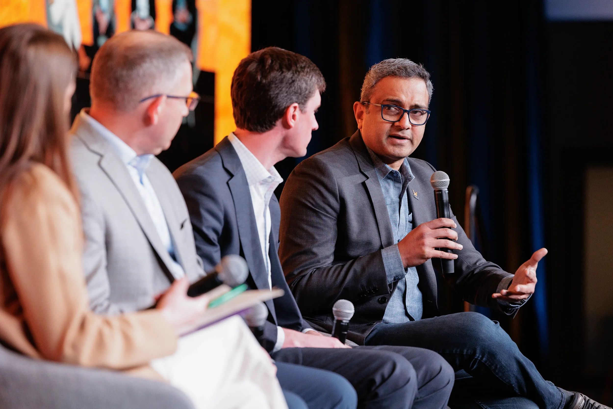 Panelist speaks into microphone and gestures while seated on stage at Orlando industry conference