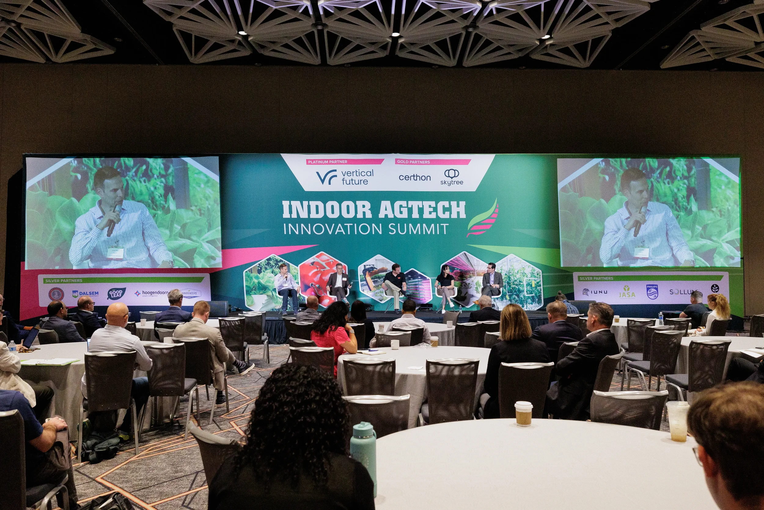 Wide view of general session with panelists on stage and attendees seated at round tables in Chicago conference ballroom