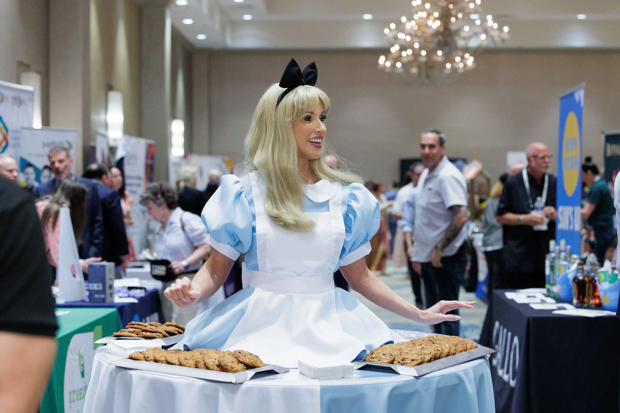 Costumed performer in blue dress presents cookies at table on Chicago corporate conference expo floor