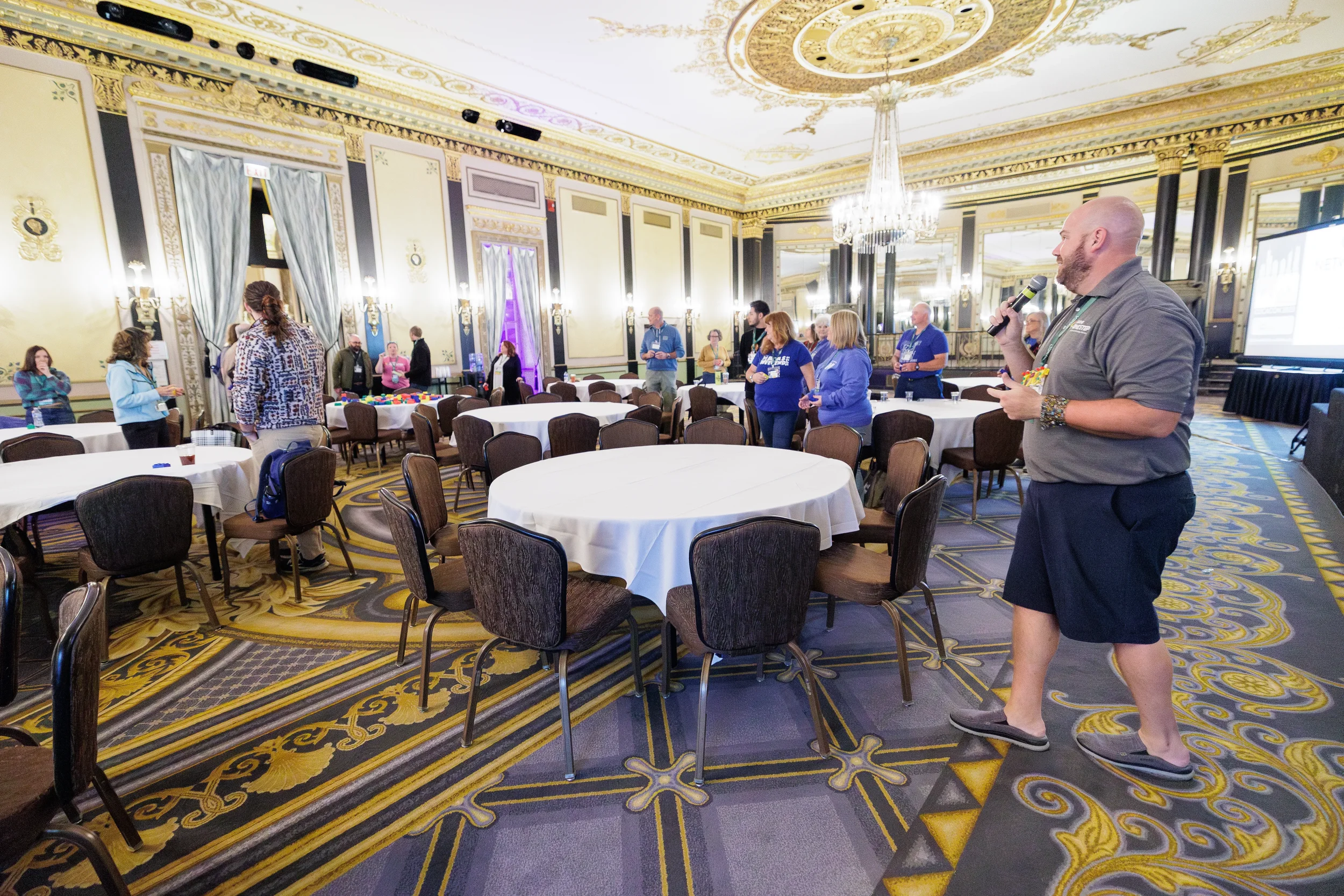 Facilitator with microphone leads activity for attendees gathered around round tables in ornate ballroom at Orlando nonprofit conference