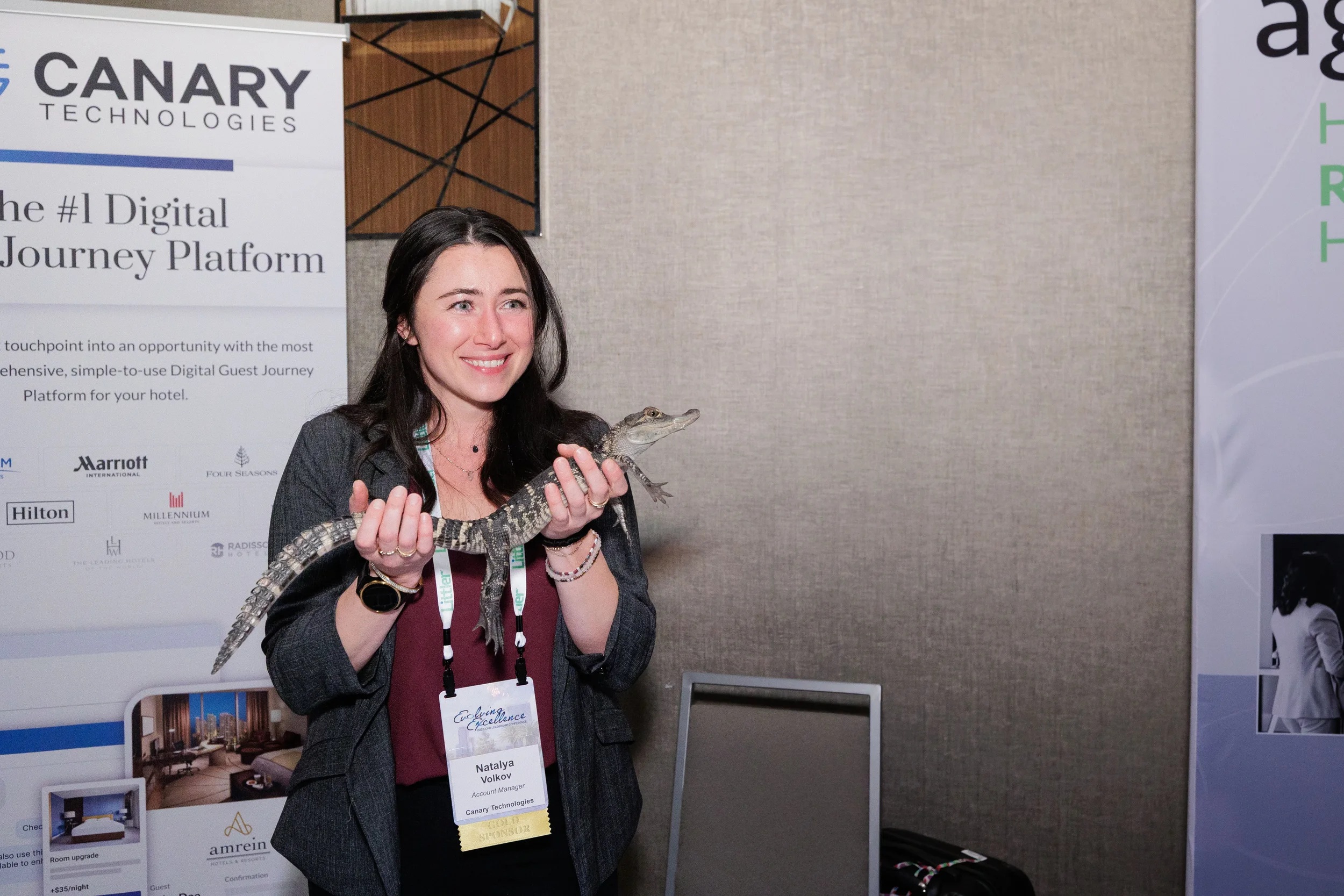 Smiling attendee with lanyard holds small alligator at exhibitor booth during Chicago industry conference