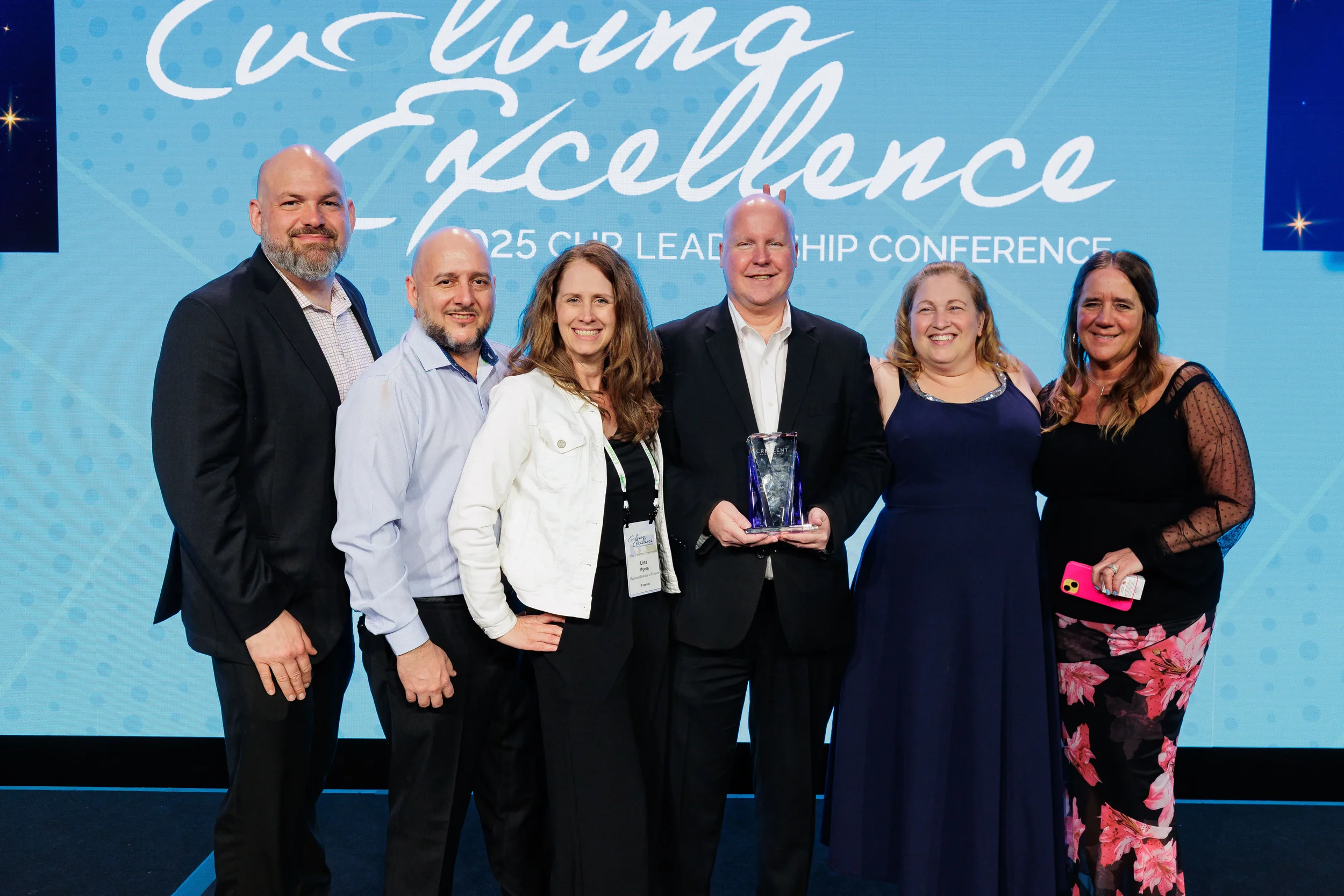 Group of six pose with crystal award on branded stage at Orlando corporate leadership conference