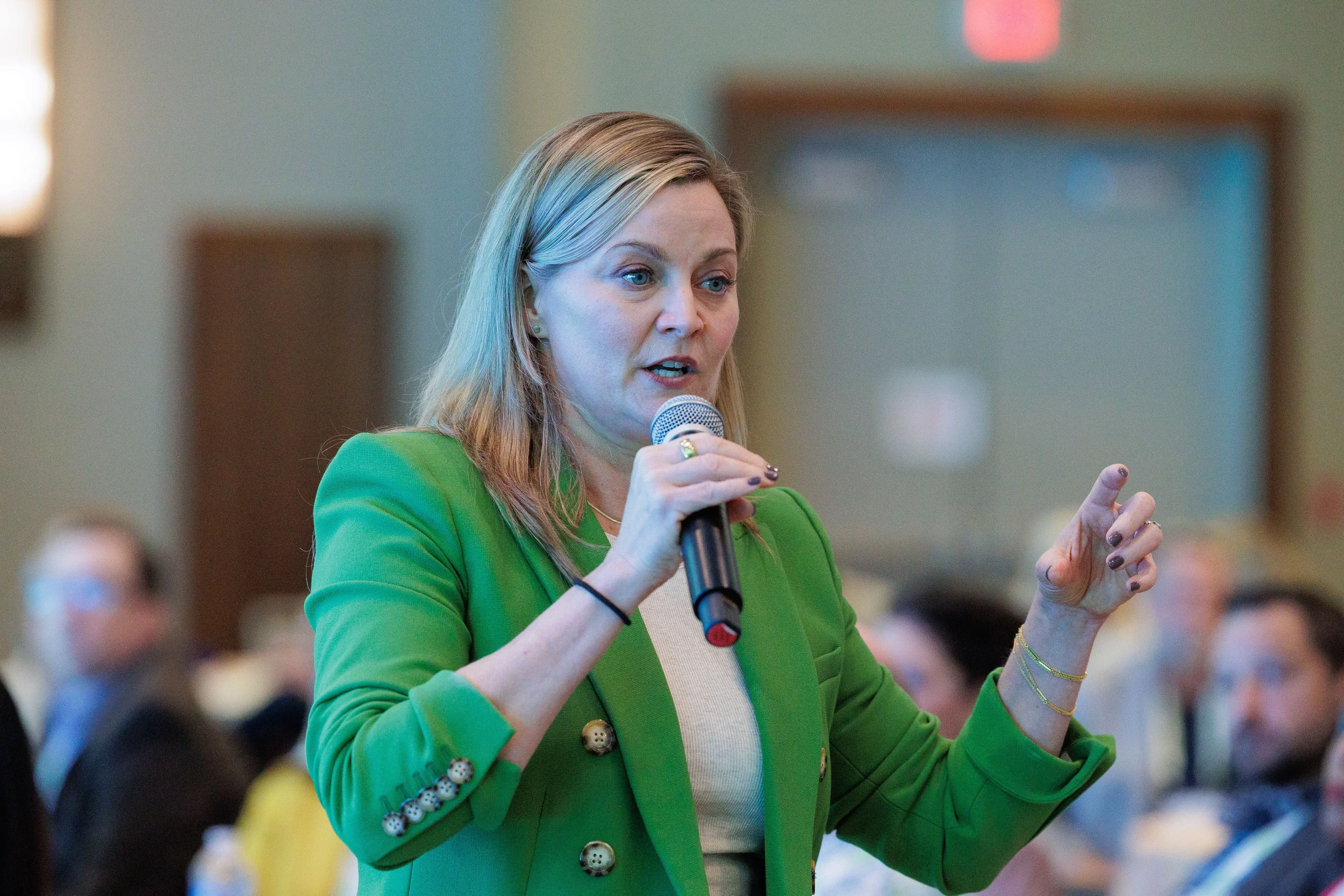 Female speaker in green blazer holds microphone and gestures while presenting at Chicago corporate conference