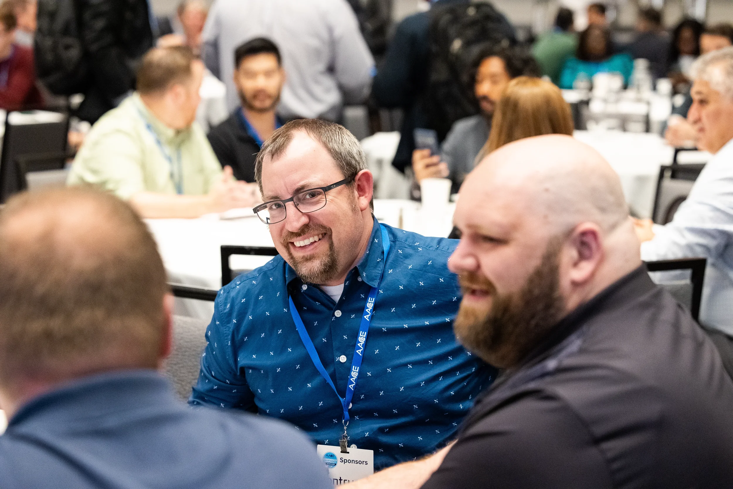 Attendees wearing conference lanyards laugh together at round table during Orlando industry conference event