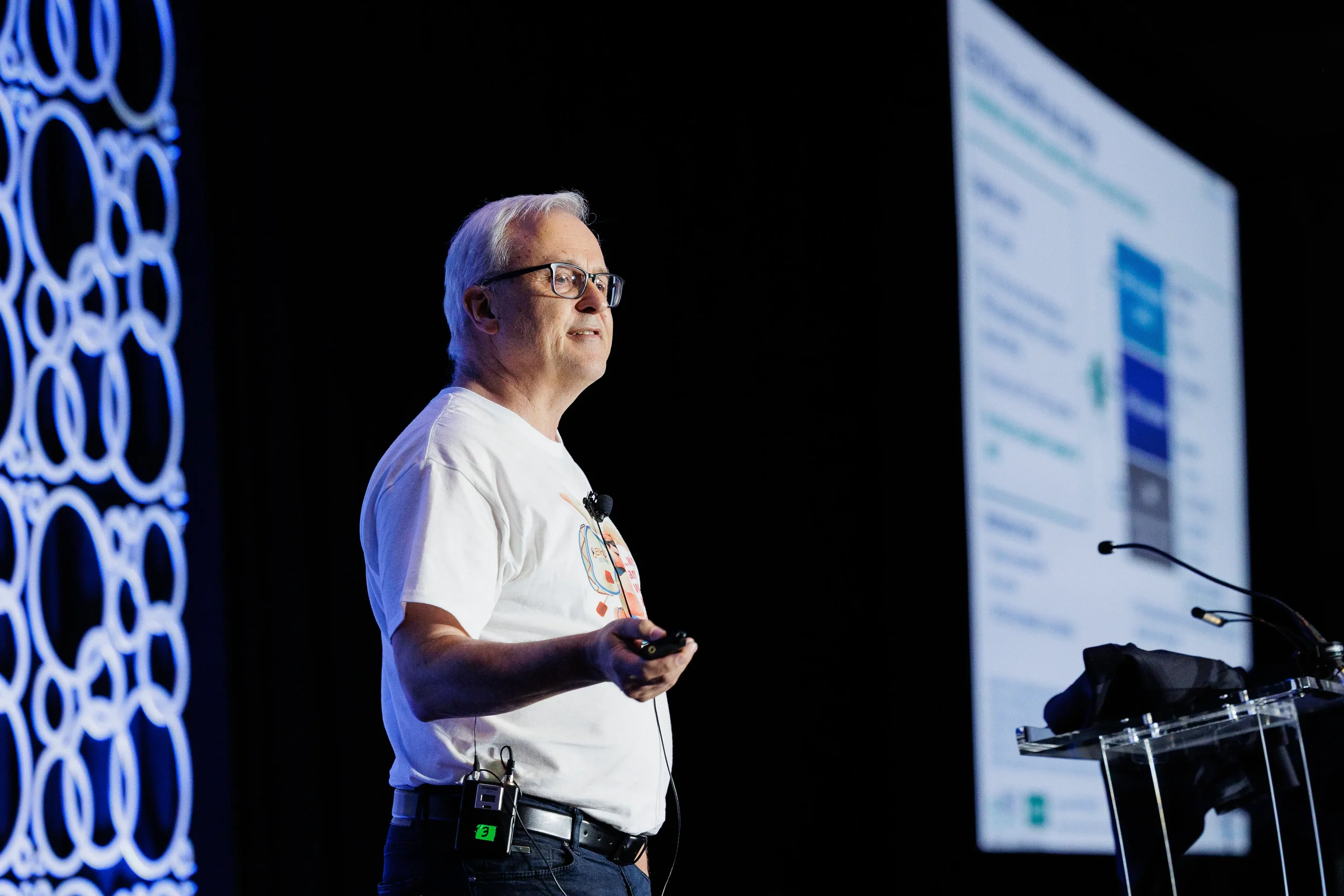 Speaker in white t-shirt presents with slide clicker on stage at Chicago industry conference