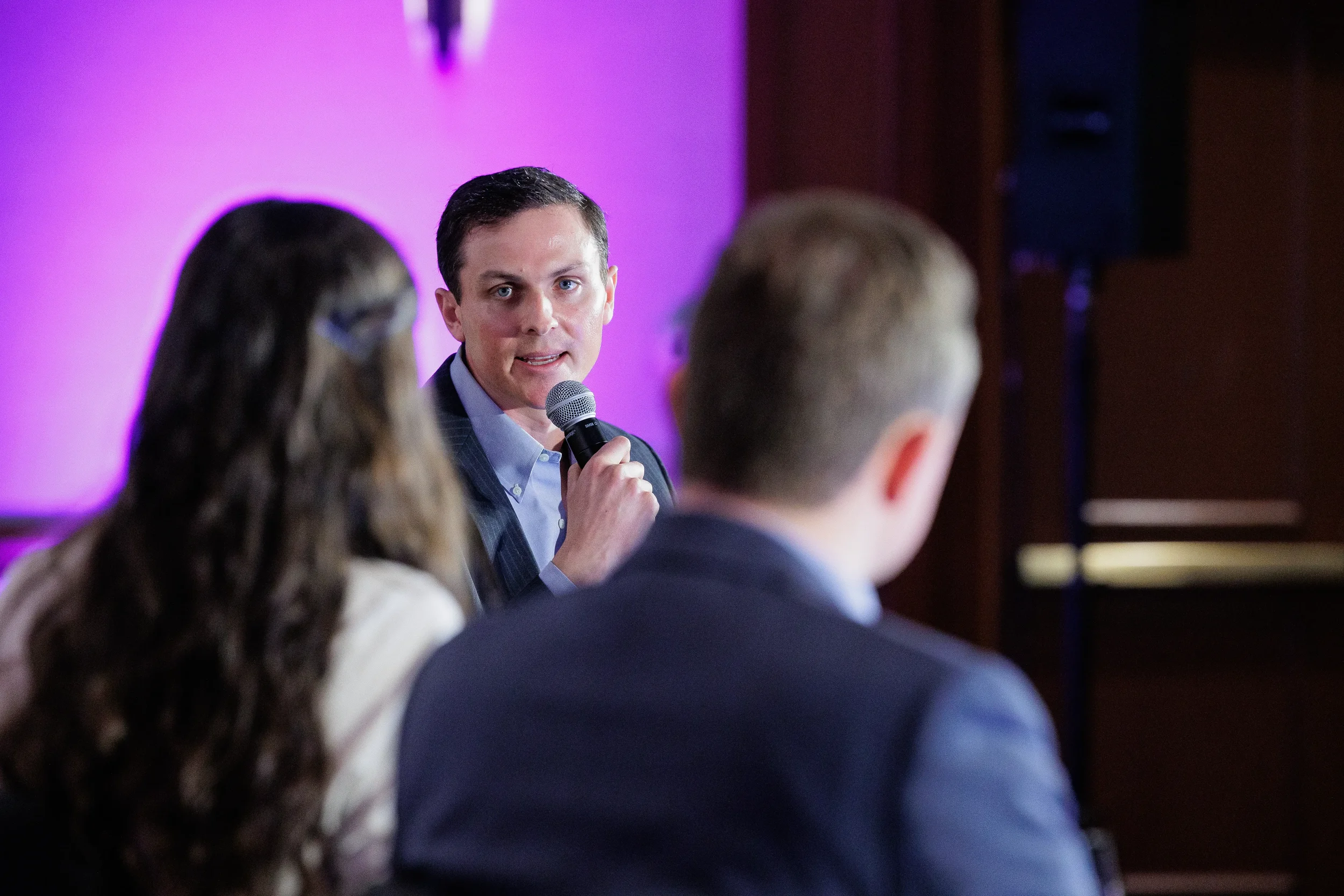 Speaker holds microphone while presenting under purple lighting at Chicago industry summit