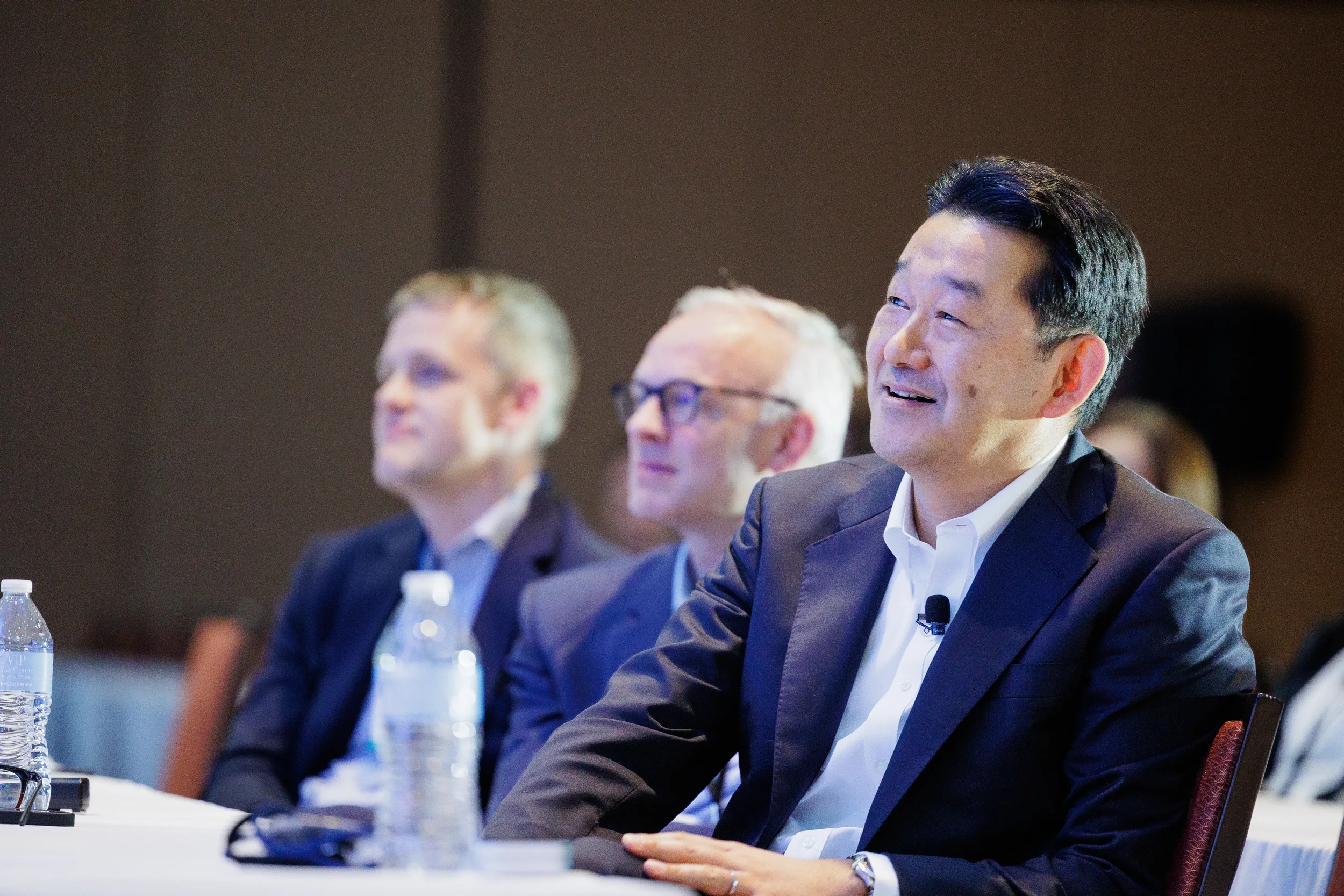 Smiling attendee watches presentation from seated table with water at Chicago corporate summit