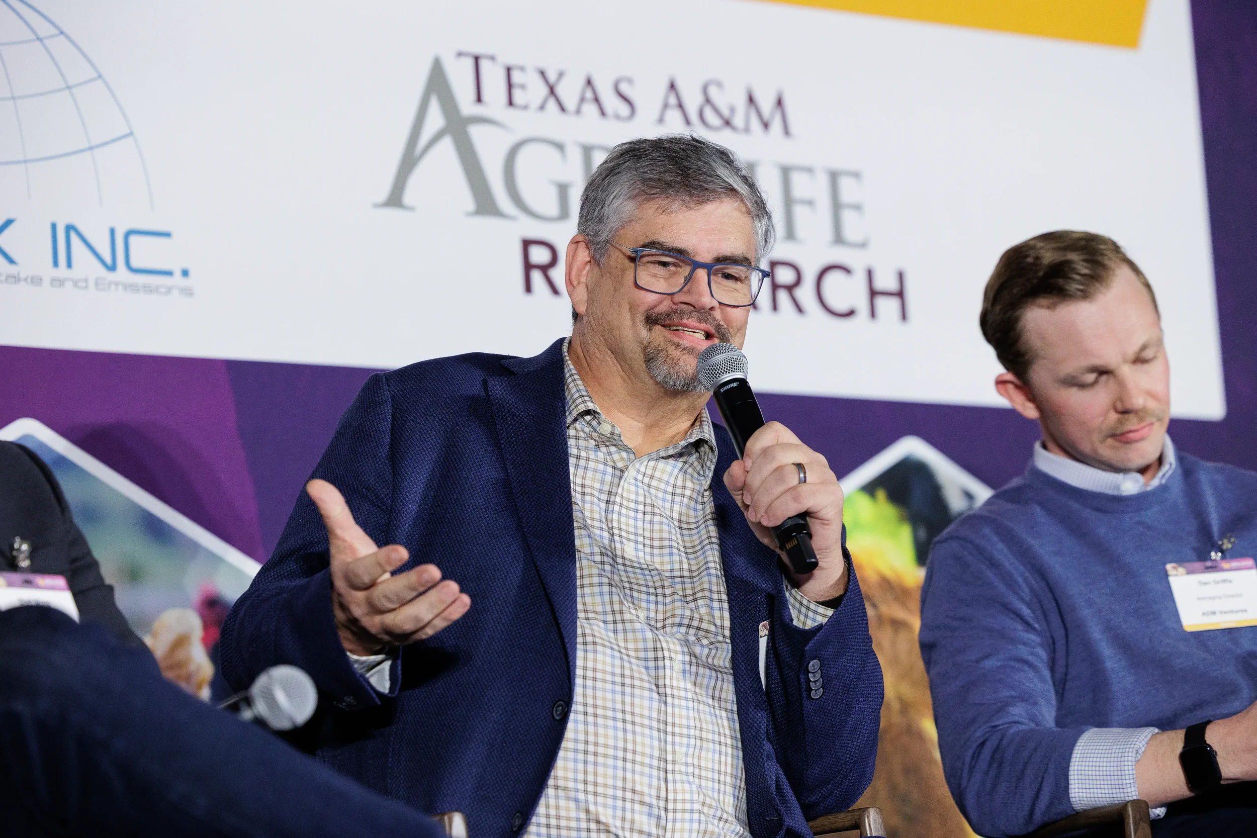 Panelist gestures while speaking into microphone during seated panel at Orlando industry conference
