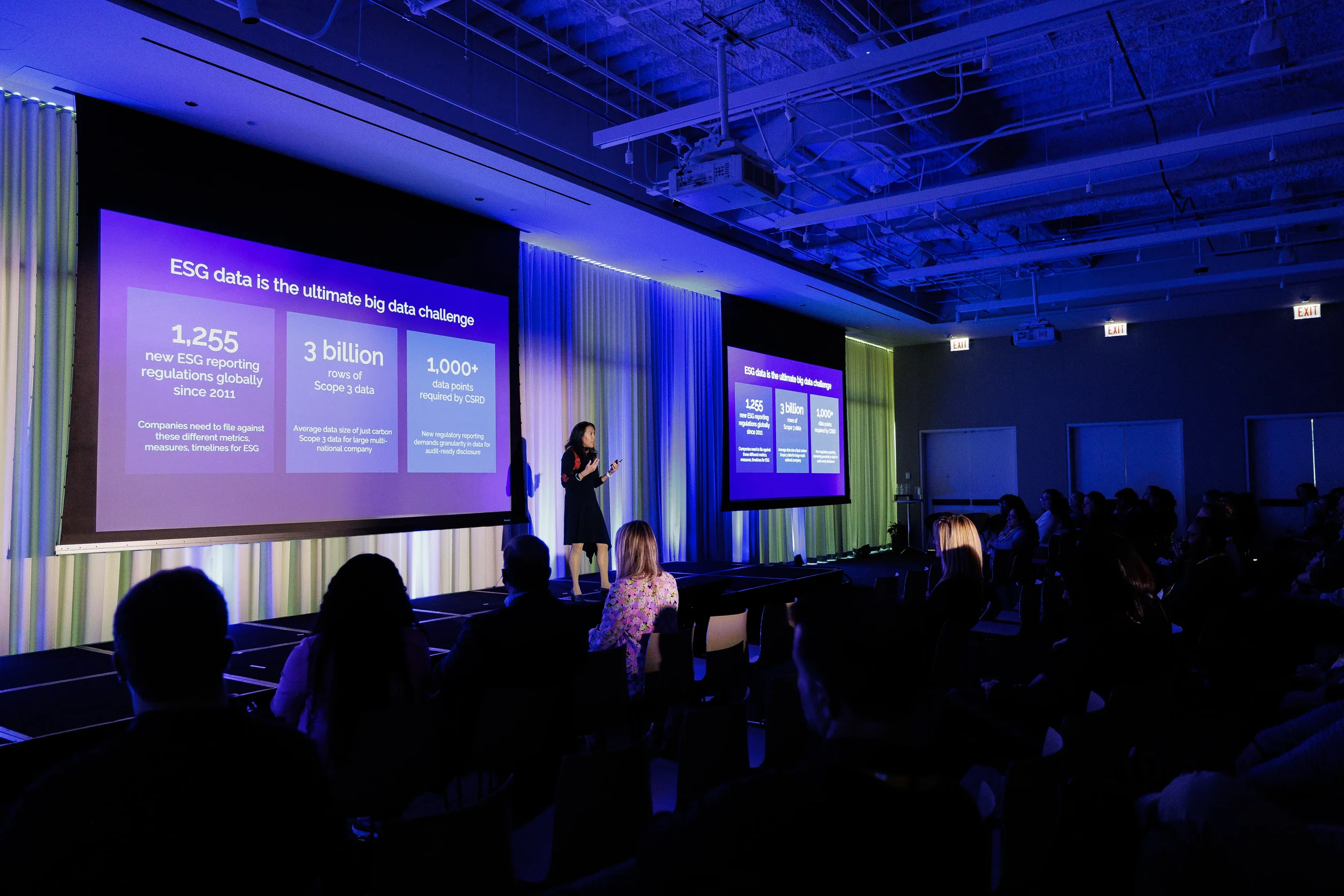 Speaker presents data slide on stage to seated audience in purple-lit room at Orlando industry conference