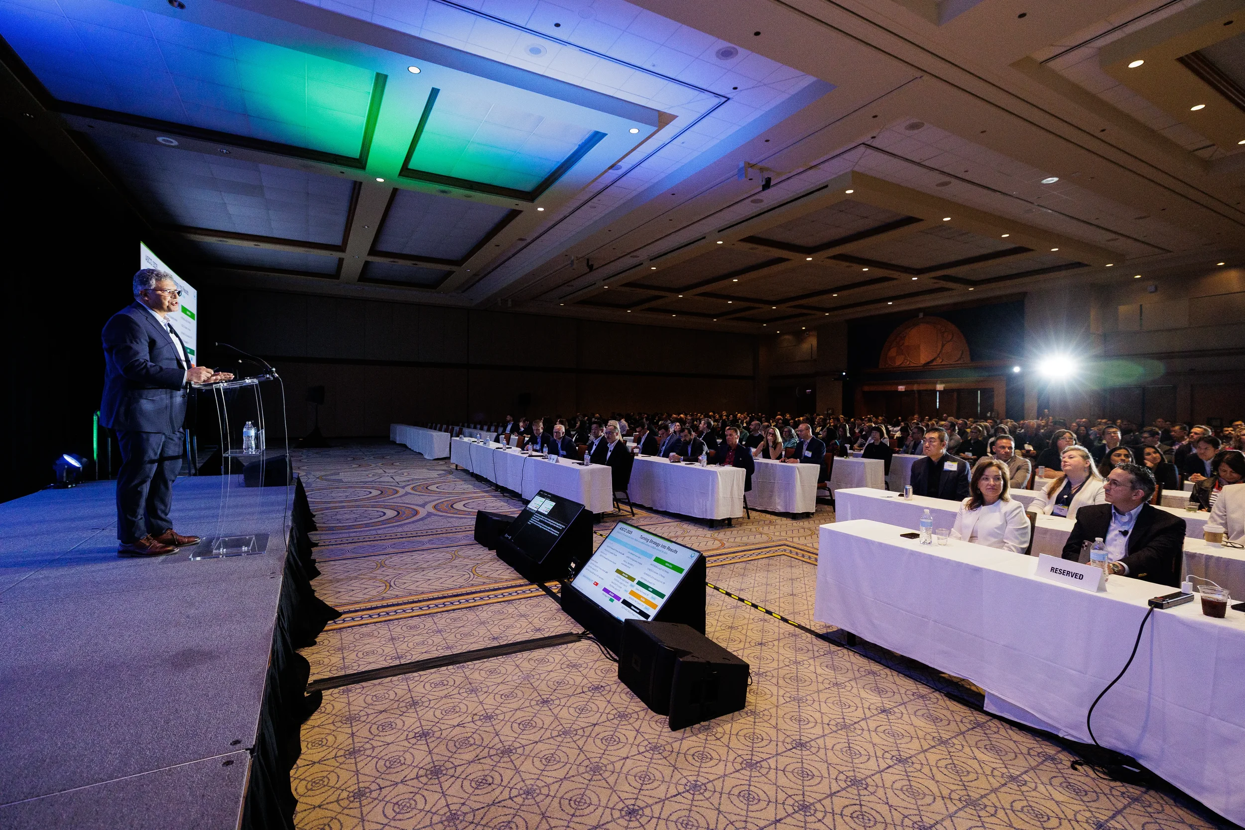 Speaker presents from podium to seated audience in ballroom at Orlando corporate conference