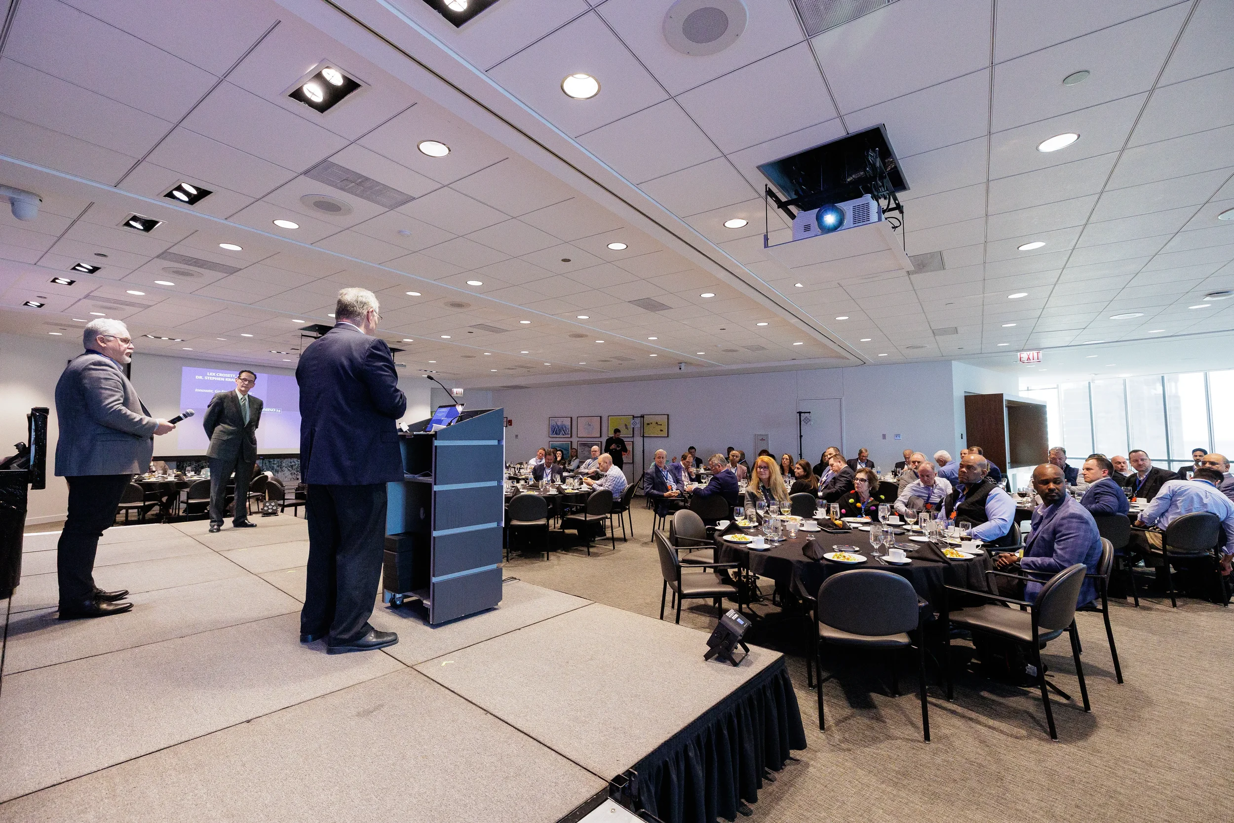 Two speakers stand at podium on stage addressing full room of attendees at Chicago corporate event